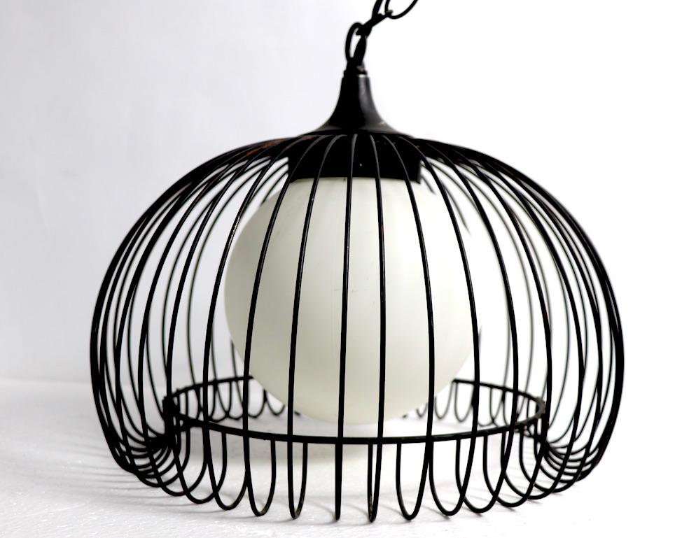 Paire de luminaires suspendus chics et élégants, chacun ayant une structure en forme de cage d'oiseau en fer qui entoure un globe blanc givré. Ces deux lampes ont été conçues à l'origine comme des lampes à orifices, et sont donc livrées avec une