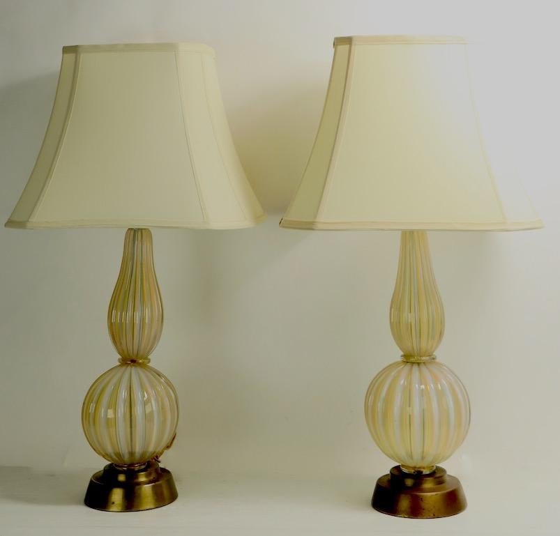 Chic pair of Italian Murano glass table lamps having ribbed bodies on metal bases. Both are in very good original, and working condition. The metal bases show cosmetic wear to finish, normal and consistent with age. Sold and priced as a pair, shades