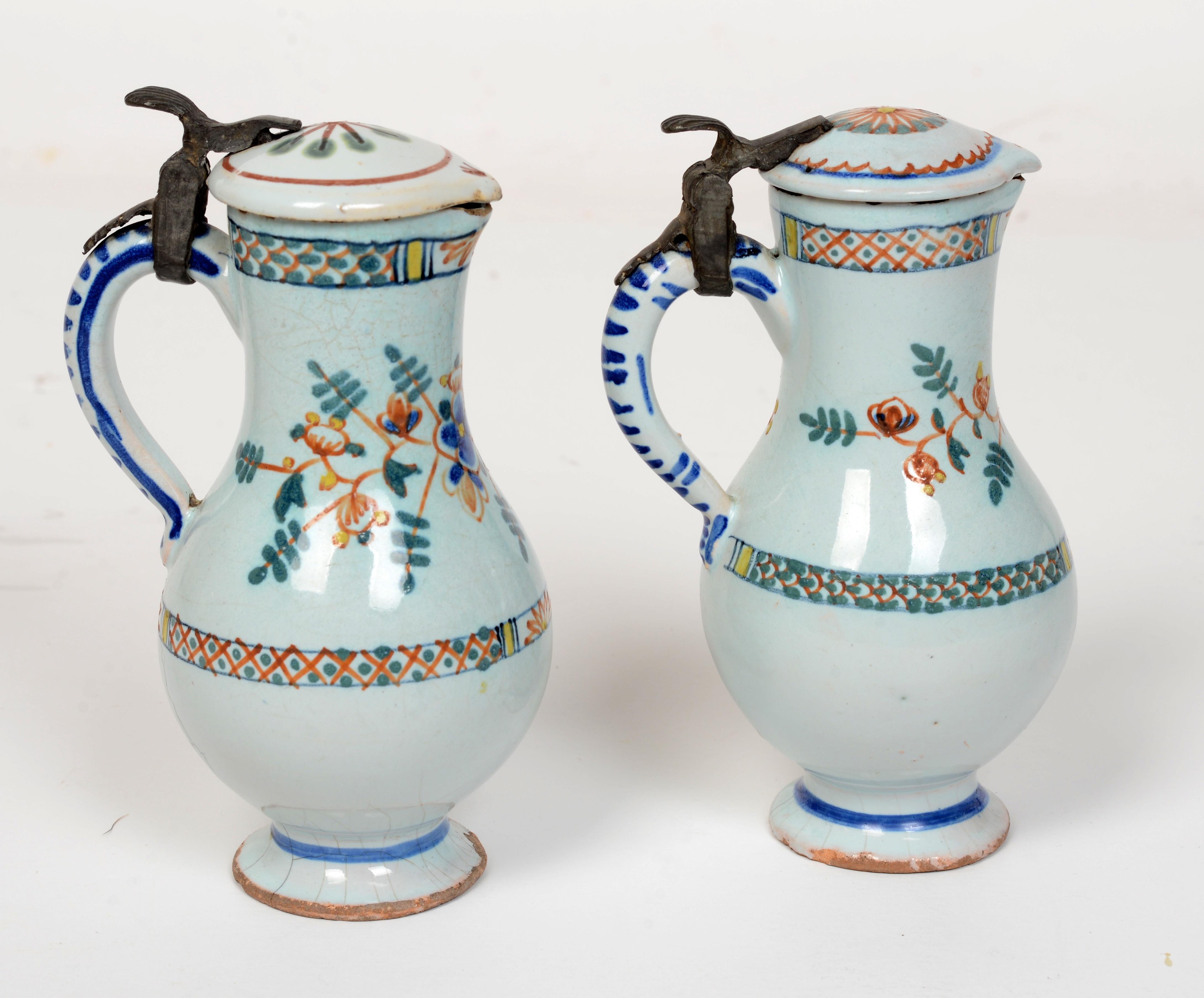 Rare Pair of 19th c French Faience Poly-Chrome Painted Small Pitchers With Hinged Lids. The pitchers are tin glazed earthenware with original lids that are attached with pewter hinges. Both pitchers have chips, crackalure and age cracks typically