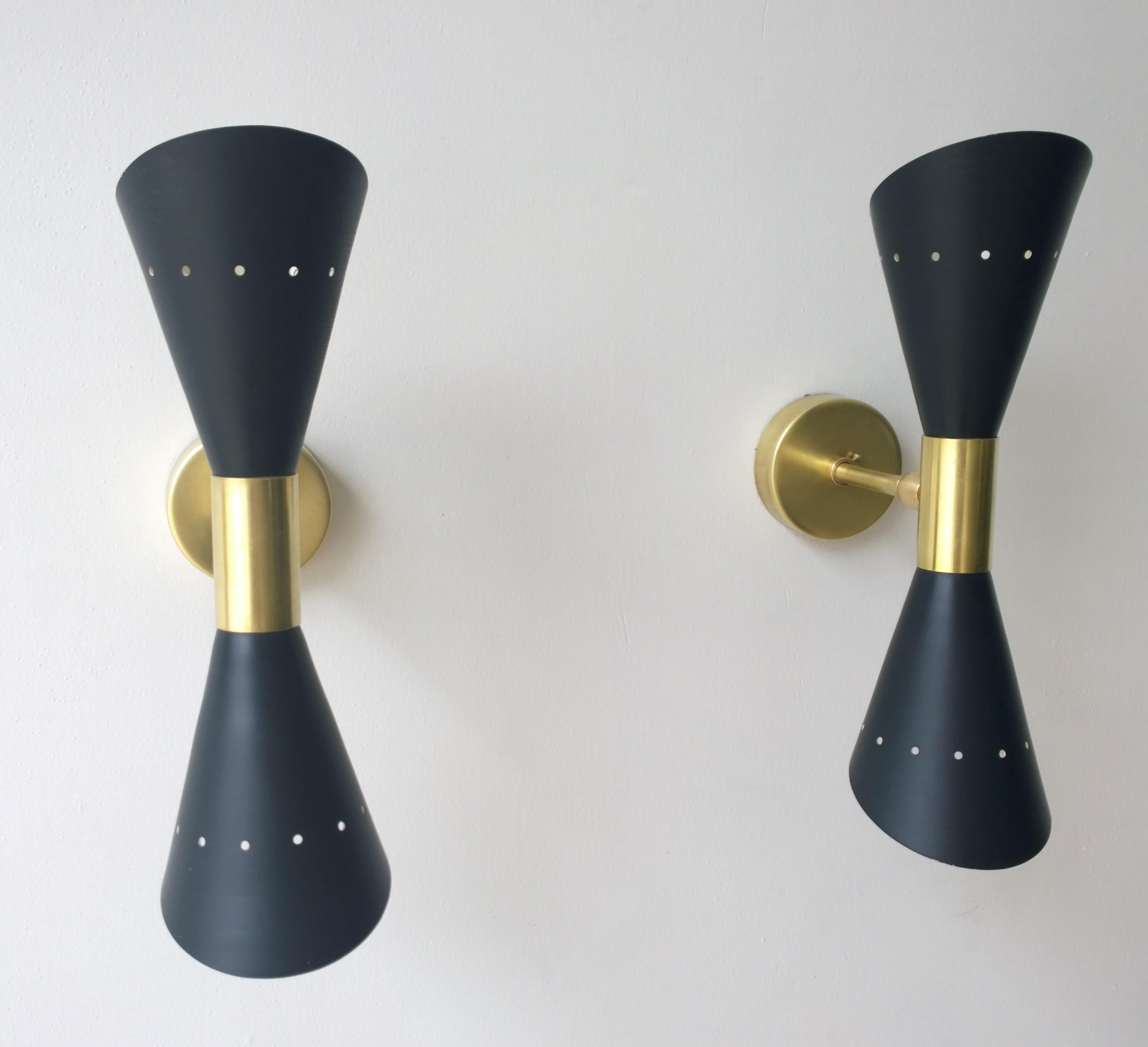 Offered is a pair of Mid-Century Modern Italian Stilnovo style enameled in black (exterior) and white (interior) steel double cone (2 candelabra each) sconces with brass hardware. Each cone has stylized perforations at each end. The brass arm