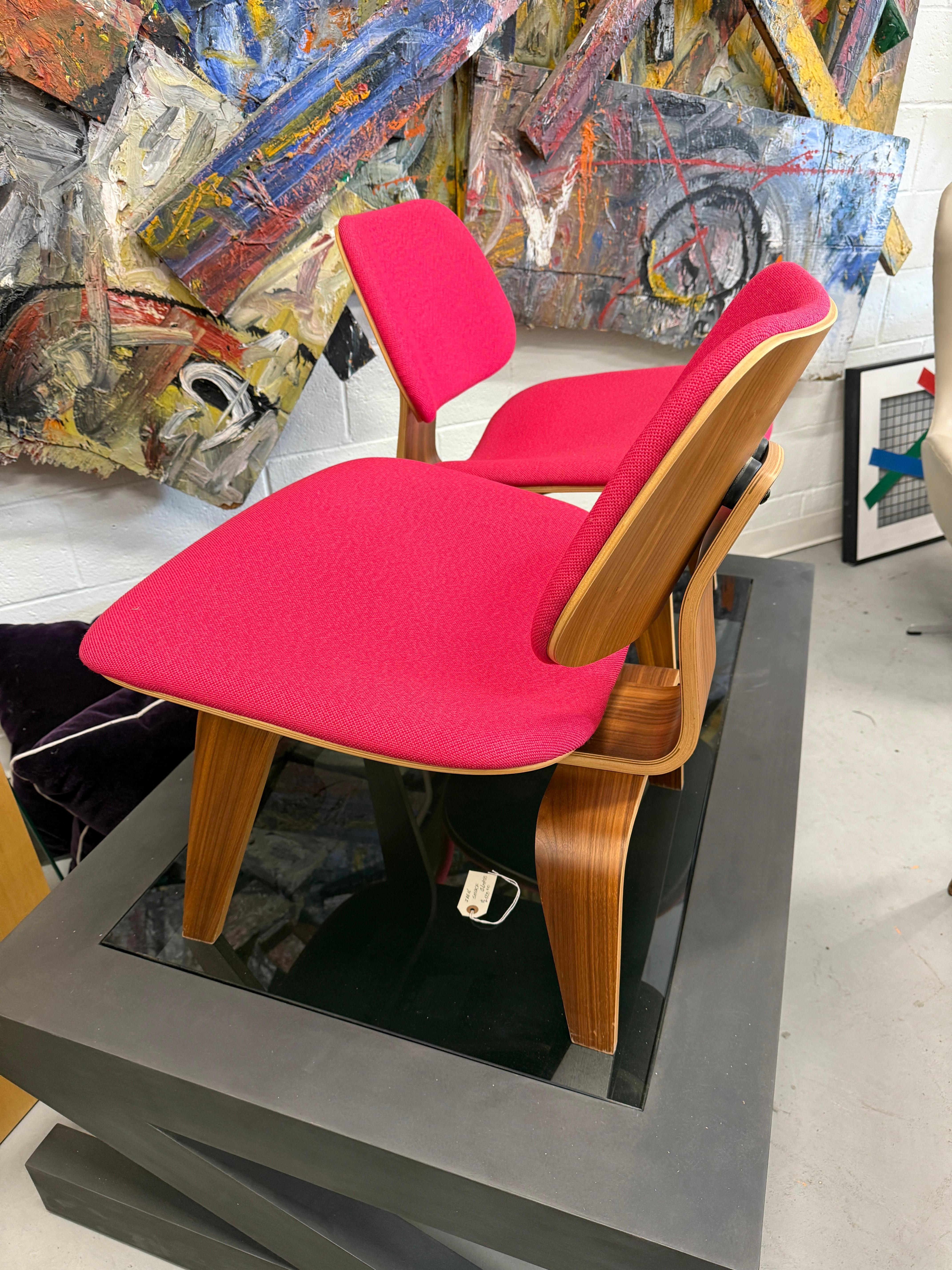 Una bellissima coppia di sedie LCW disegnate dagli Eames e prodotte da Herman Miller. Sono rivestite di un meraviglioso colore rosa/fuschia. Le sedie sono impiallacciate in noce. Hanno indicato le etichette Herman Miller e la data di produzione del