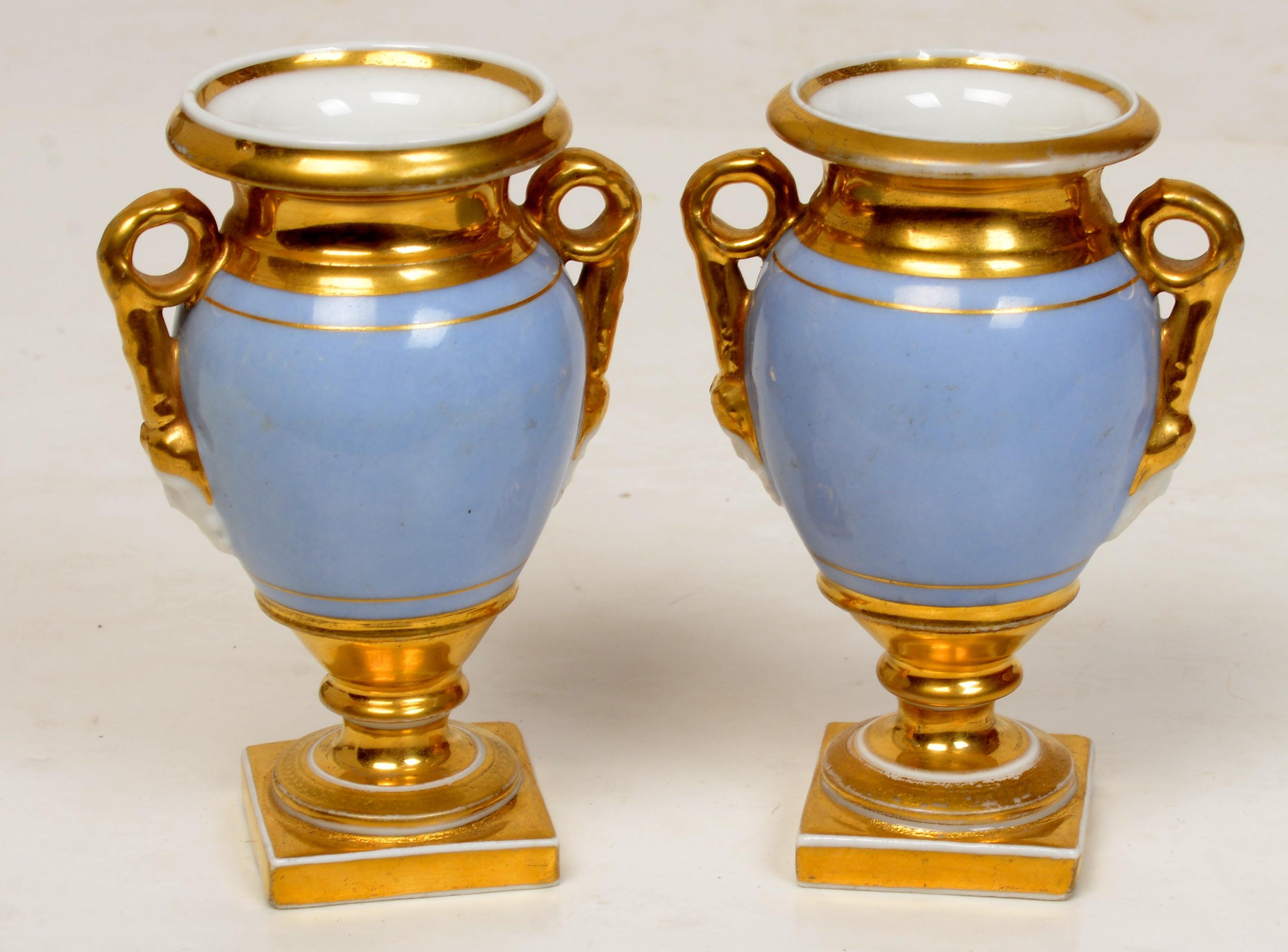 Pair of Old Paris Miniature, Gilt Decorated Footed Urns with garden scenes, c1800. Miniature urns of this type are rare and the decoration is exceptional. The urns have bolted construction with scrolling handles and molded face mask terminals. The