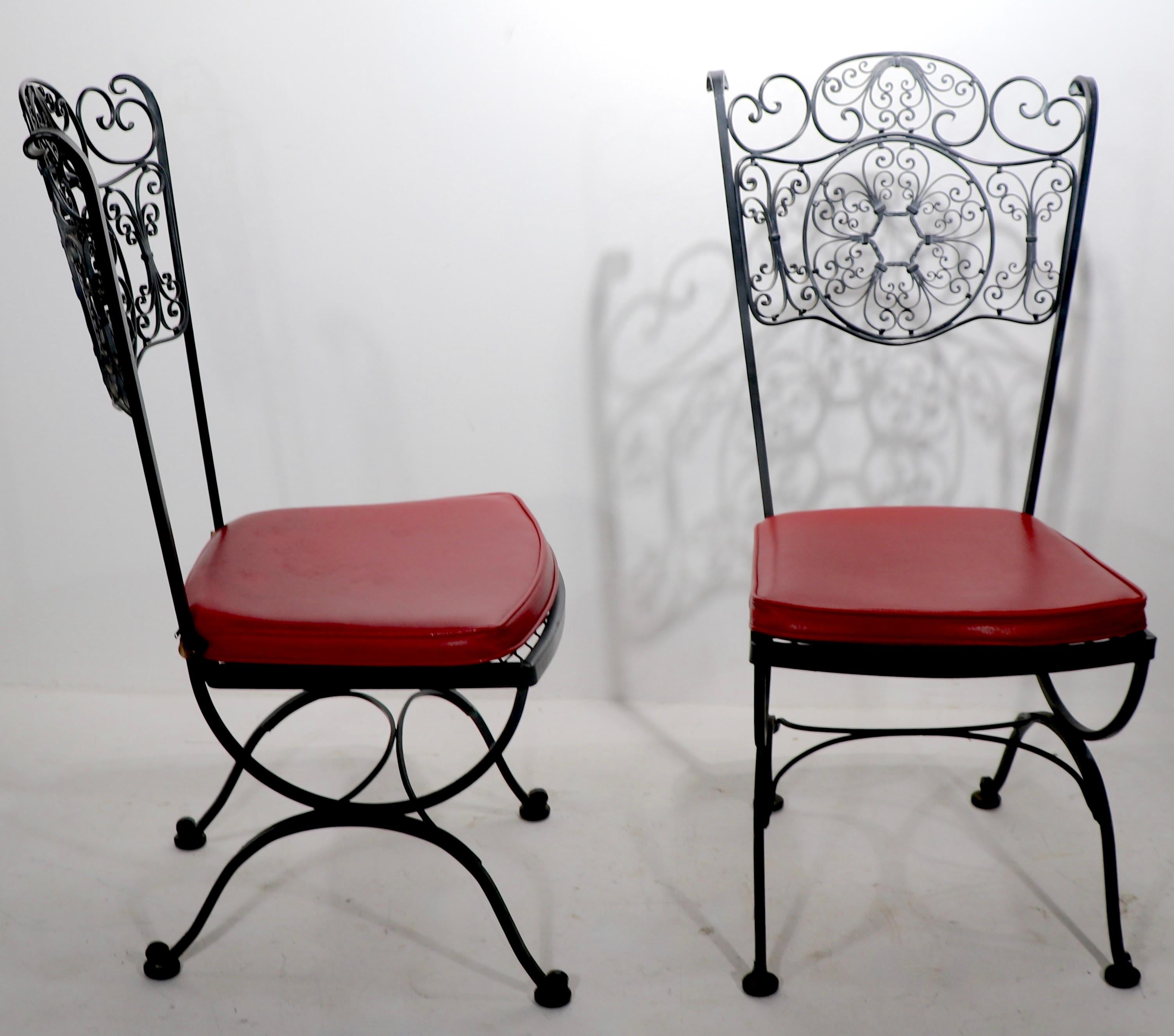 Pair ornate wrought iron dining chairs, with original vinyl seats. Both are in very fine, ready to use condition, retaining Lee Woodard labels. Offered and priced as a pair.