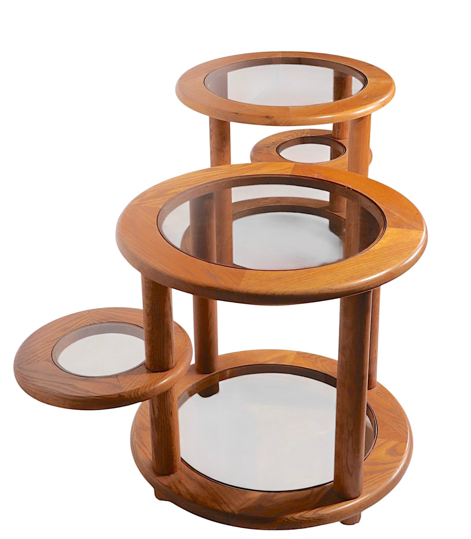 Chic and  stylish pair of mechanical disk form three tier side, or end tables, constructed of solid oak frames with tinted glass insert tops. The tables feature three circular stable surfaces, the middle surface rotates on a vertical pole form table