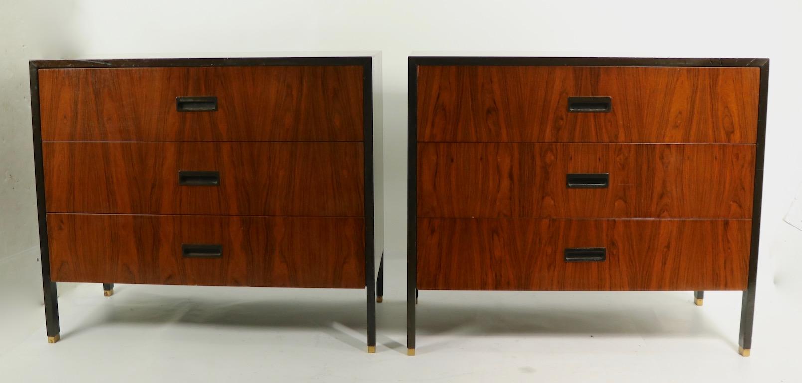 Pair of tailored chests designed by Harvey Probber, having rosewood drawer fronts, tops and sides with dark mahogany trim, and legs, with brass feet. Both are in good, original condition, showing some cosmetic signs of age and use. Each dresser has