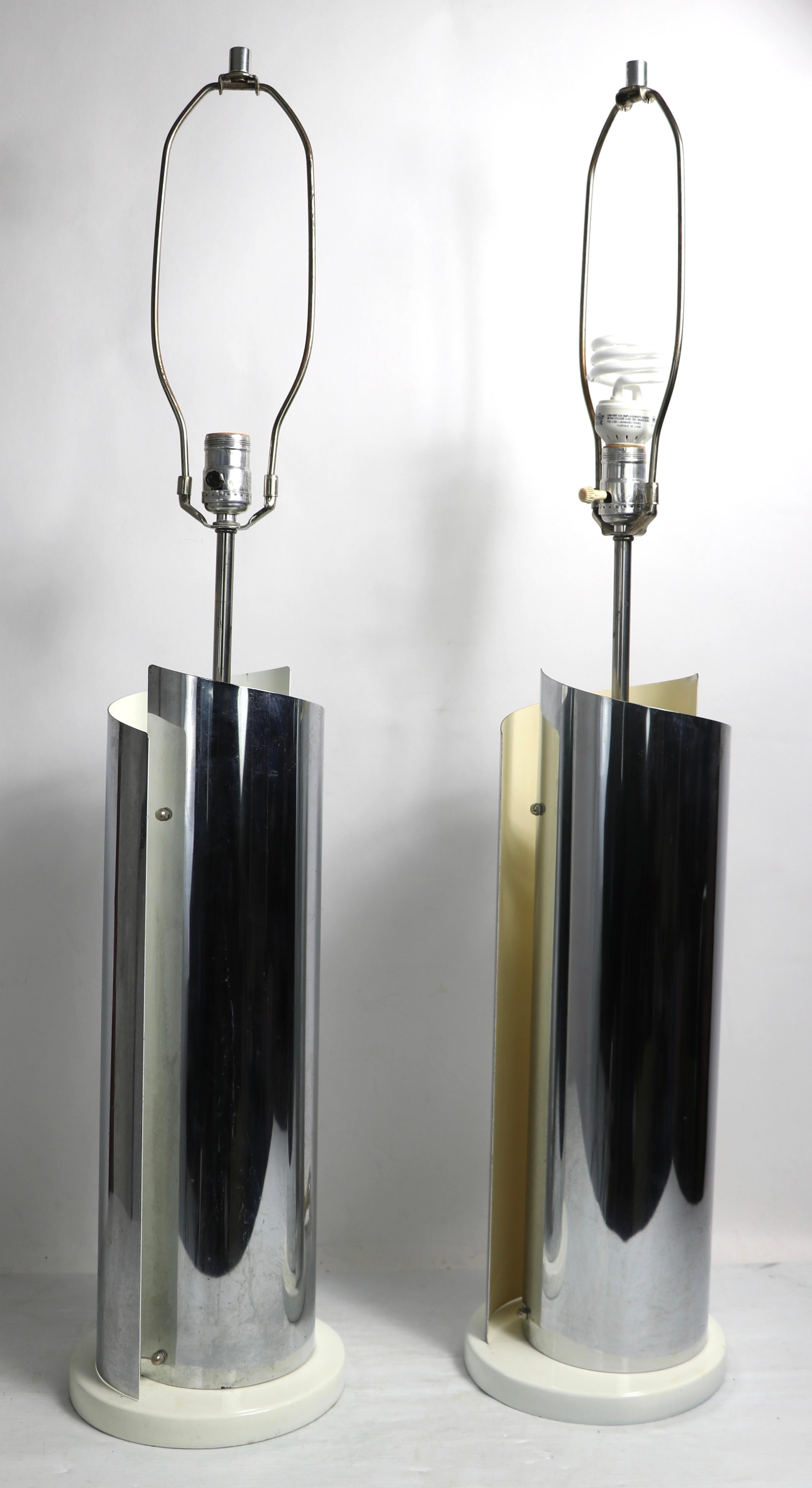 Pair of chrome table lamps having interlocking curved elements with white interiors. Each lamp features an inner socket, and an upper socket. The white paint finish one one lamp has patinated to a warmer color than the other, both are in original