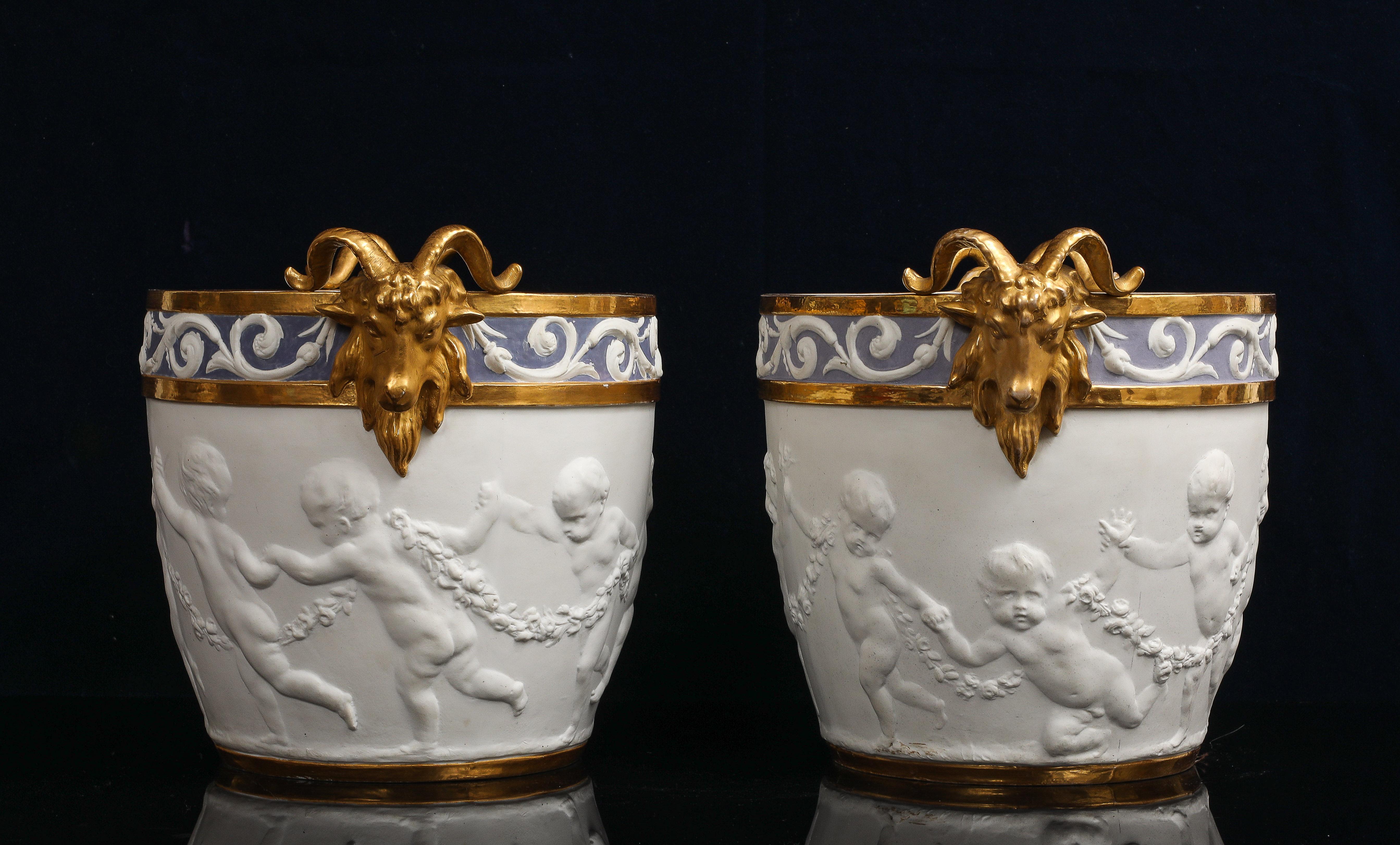 Une grande paire de centres de table/vases/pots à cendres en porcelaine biscuit de Sèvres décorés de putti avec des poignées en tête de bélier dorées.  
Chaque vase est de forme cylindrique, s'affinant légèrement à la base et présentant deux anses