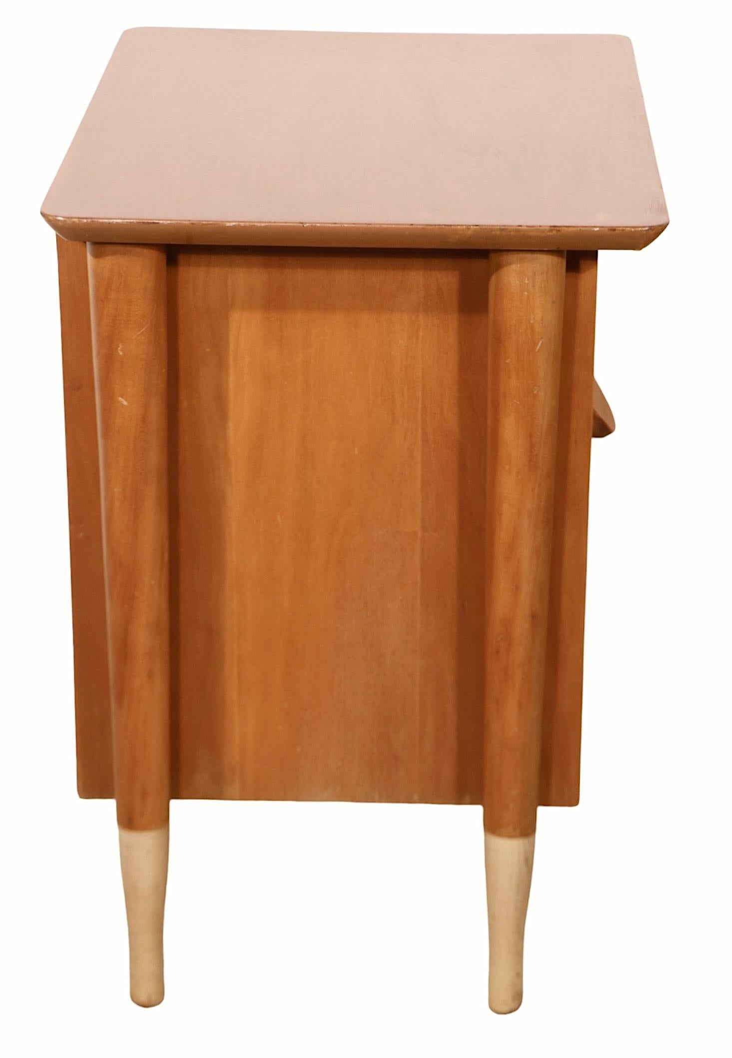 Stylish pair of night stands by Basic Witz, made in the USA, circa 1950's. The night tables feature an exposed architectural frame with an overhanging bevelled top and tapering pole legs and contrasting light tone feet. The drawers also have a two