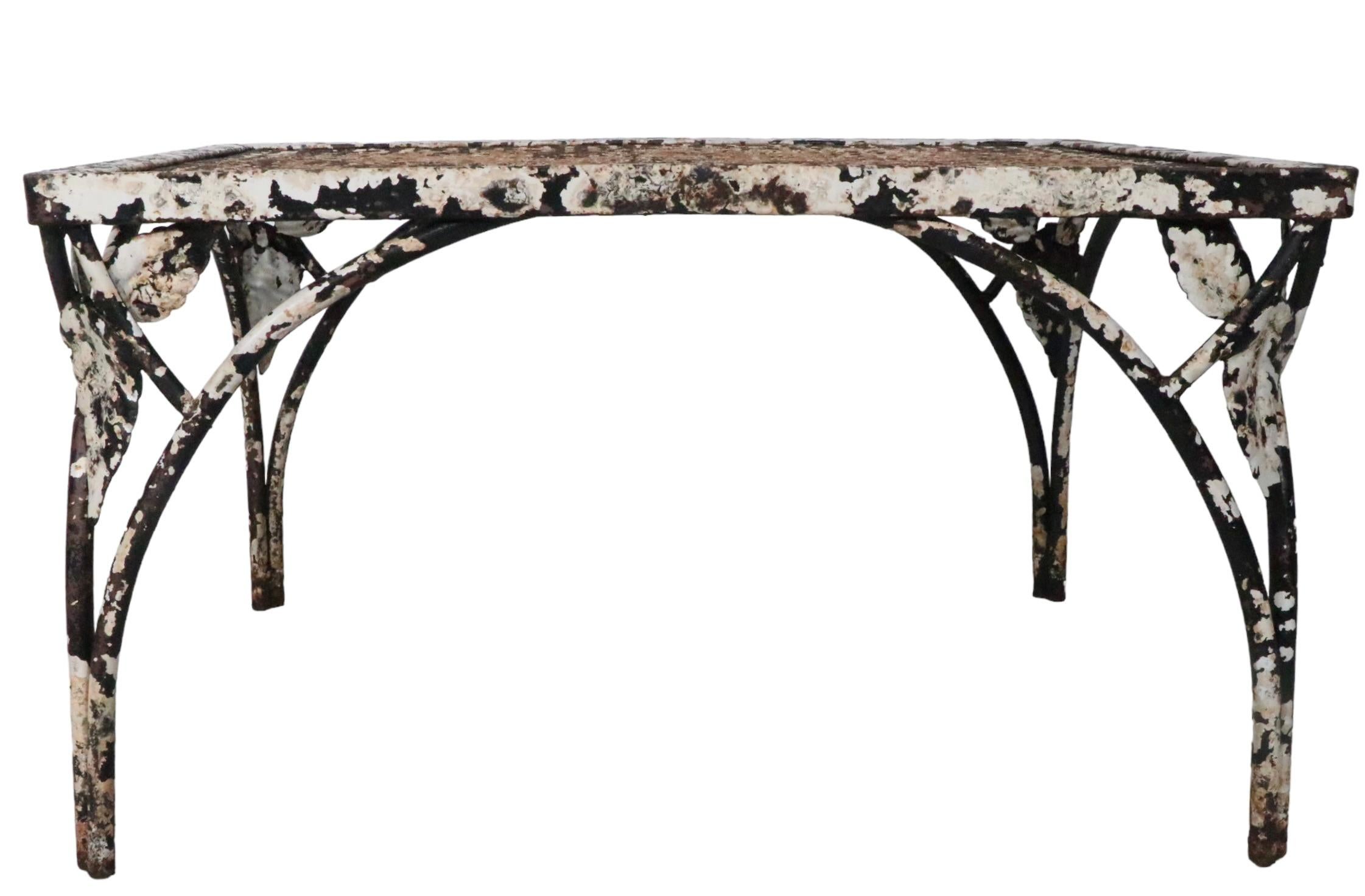 Pair. wrought iron garden, poolside, patio tables attributed to the Woodard Furniture Company, having wrought iron bases with foliate decorations, and metal mesh tops. Both tables are structurally sound and sturdy, both show considerable cosmetic