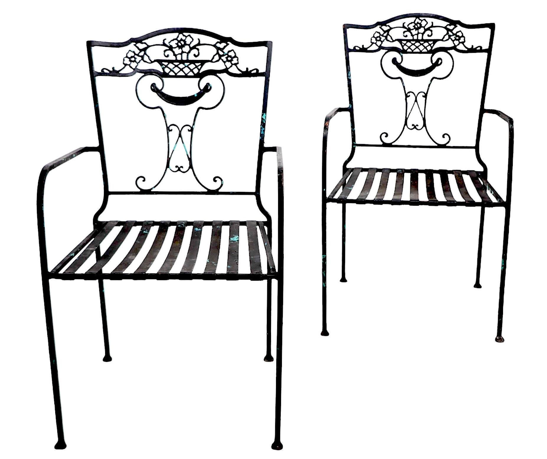 Chic pair of vintage wrought iron garden, patio, or  poolside, dining height  arm chairs, possibly by Salterini, Woodard, Leinfelder etc, unsigned. 
 The chairs feature a decorative backrest having a floral basket motif  top, above a neoclassical