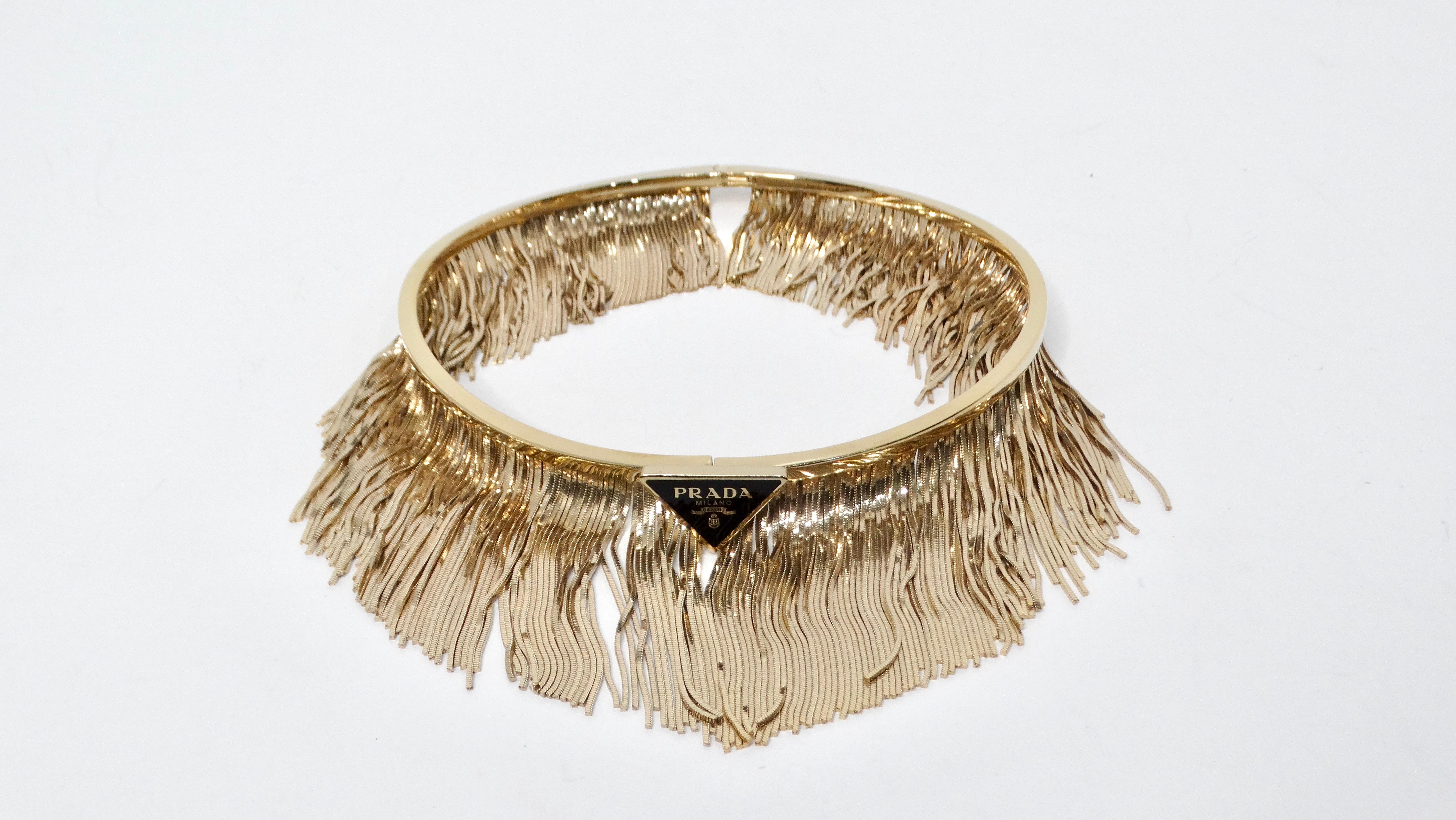 The Prada 14k Gold Plated Fringe Choker exudes luxurious elegance with its intricate design and modern flair. This statement piece features a sleek 14k gold-plated choker adorned with shimmering gold-plated fringes that gracefully sway with every