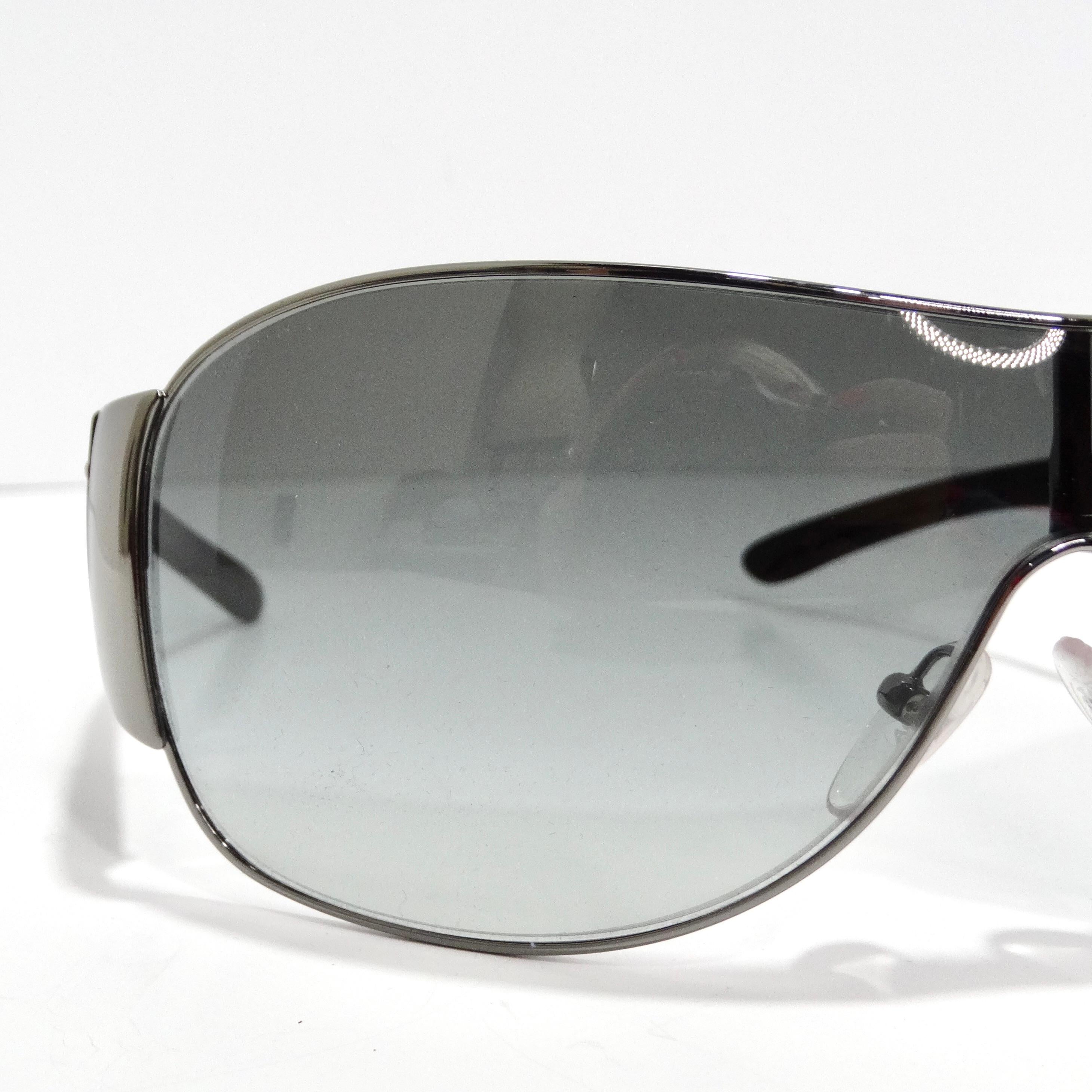 Die Prada 1990s Black Shield Sonnenbrille ist der Inbegriff des 1990er-Chics. Diese klassische Sonnenbrille im Shield-Stil verfügt über dünne silberfarbene Ränder, schlichte schwarze Bügel mit silberfarbenen Prada-Logos und blau-graue
