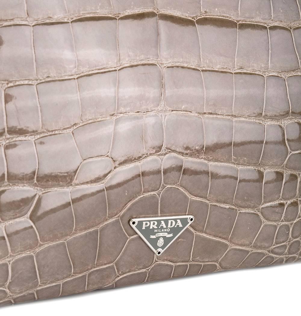 Magnifique sac fourre-tout Prada en cuir crocodile gris clair. Il est doté de poignées supérieures:: d'une fermeture à pression supérieure:: d'un compartiment interne principal:: d'une plaque de logo en métal argenté et d'un cuir à effet brillant.