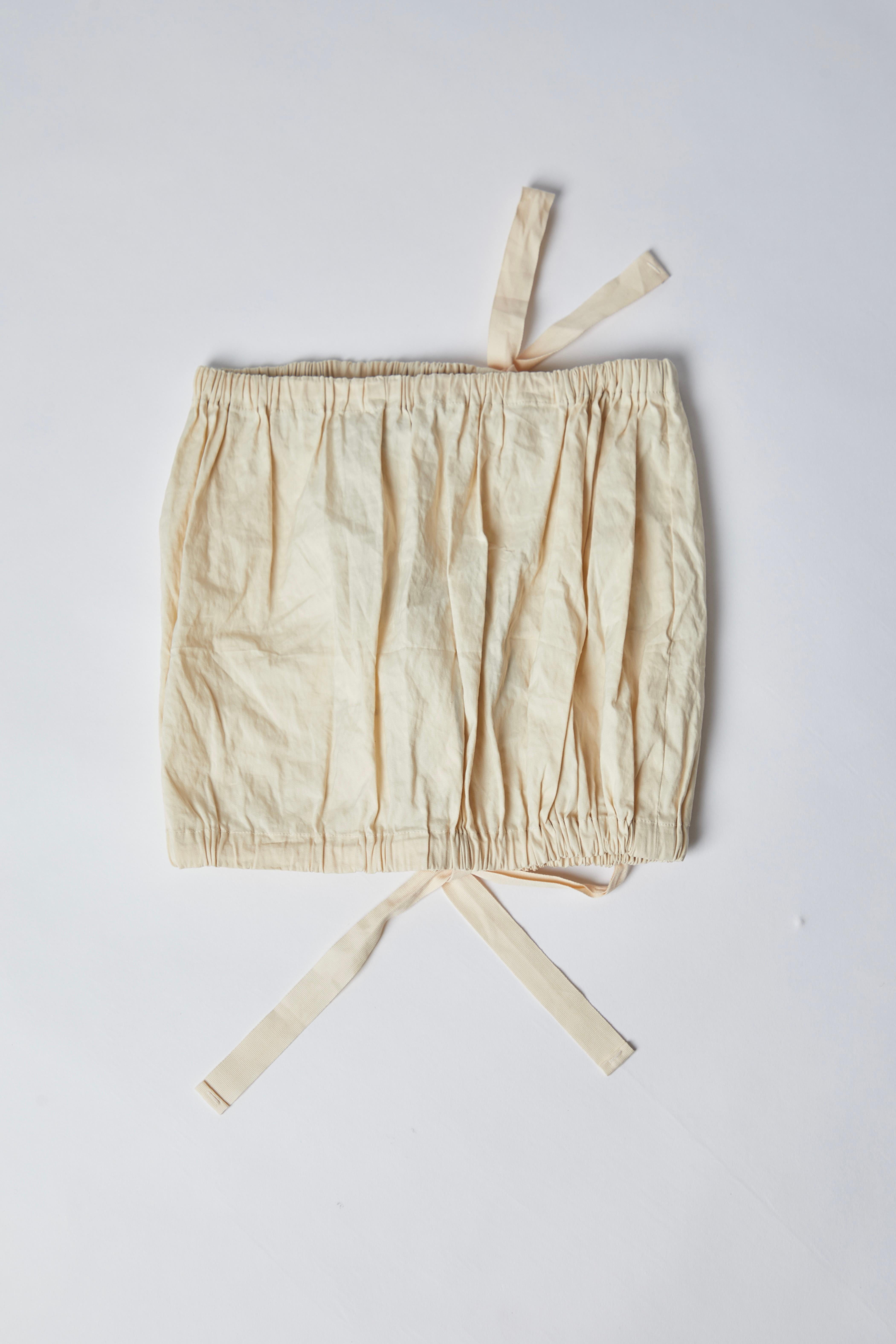 Piece Description: This Prada beige tube top from the 2009 Spring/Summer collection is a stylish, minimalist piece designed with a wrinkled texture for a relaxed yet polished look. It features a charming bow detail at the front, adding a feminine