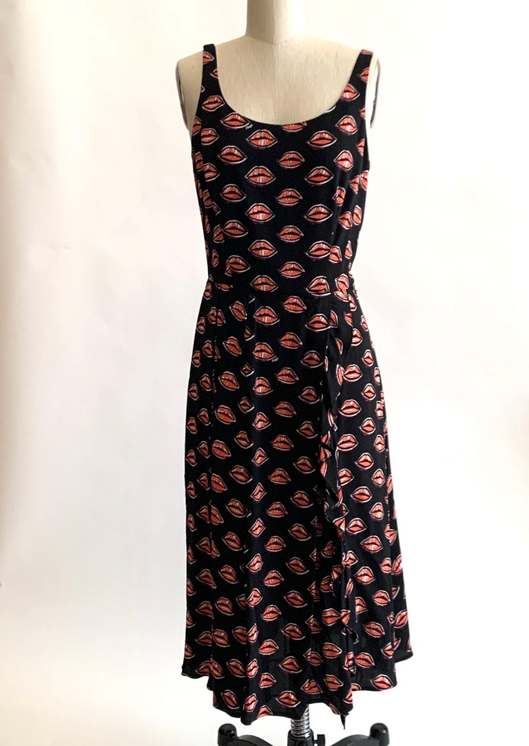 Prada black sleeveless dress in red and white scribble lip print. Small Prada signatures throughout.  Asymmetrical pleated draping and vertical ruffle detail at skirt. Side zip and hook and eye. 

98% viscose, 2% elastane.
Bodice lined in 100% silk,