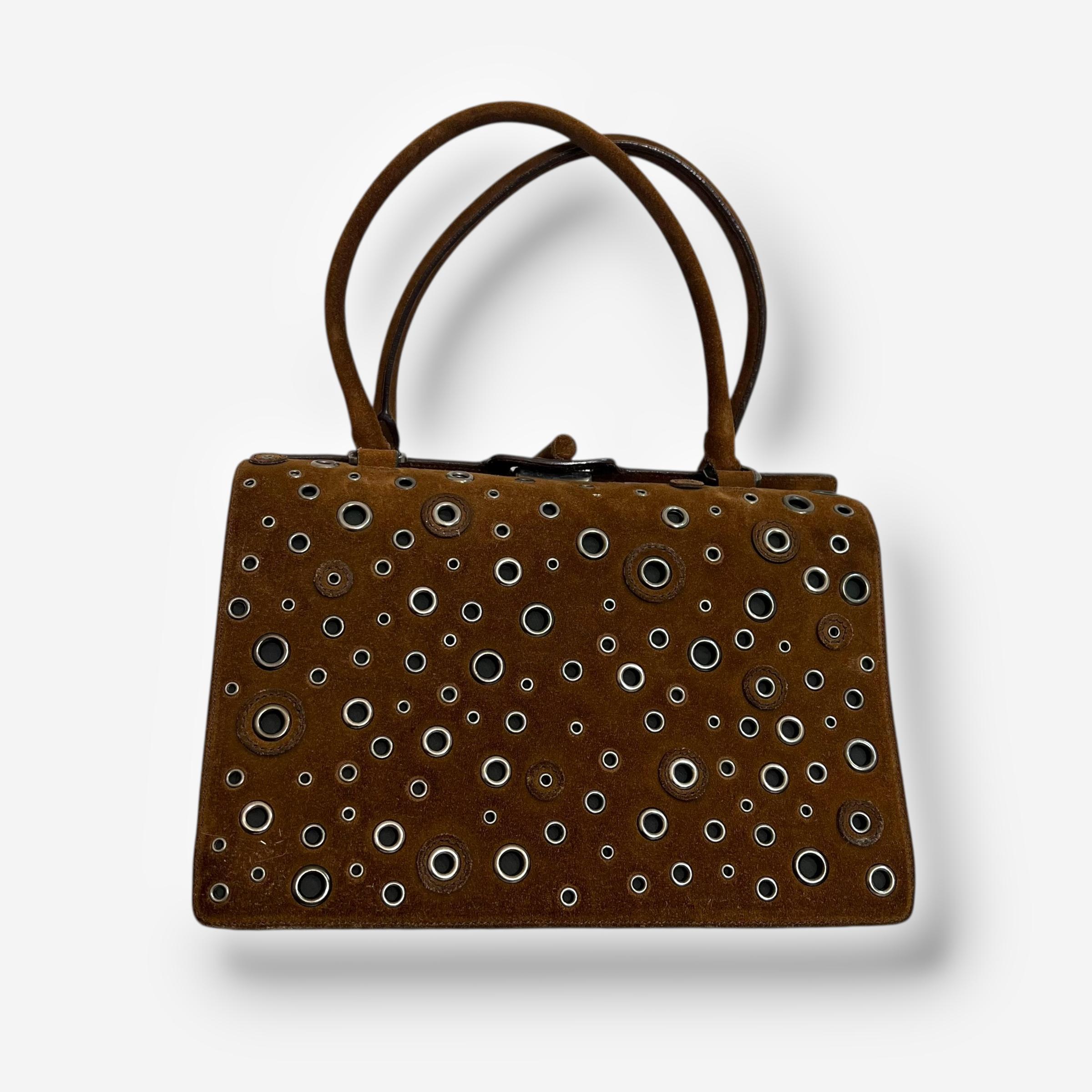 

Un llamativo bolso vintage de Prada, fabricado en ante marrón y adornado con un diseño de ojales con ojales. Su estructura se abre para revelar un interior forrado en piel de color naranja vivo, que incluye un monedero con cierre de pestillo y un