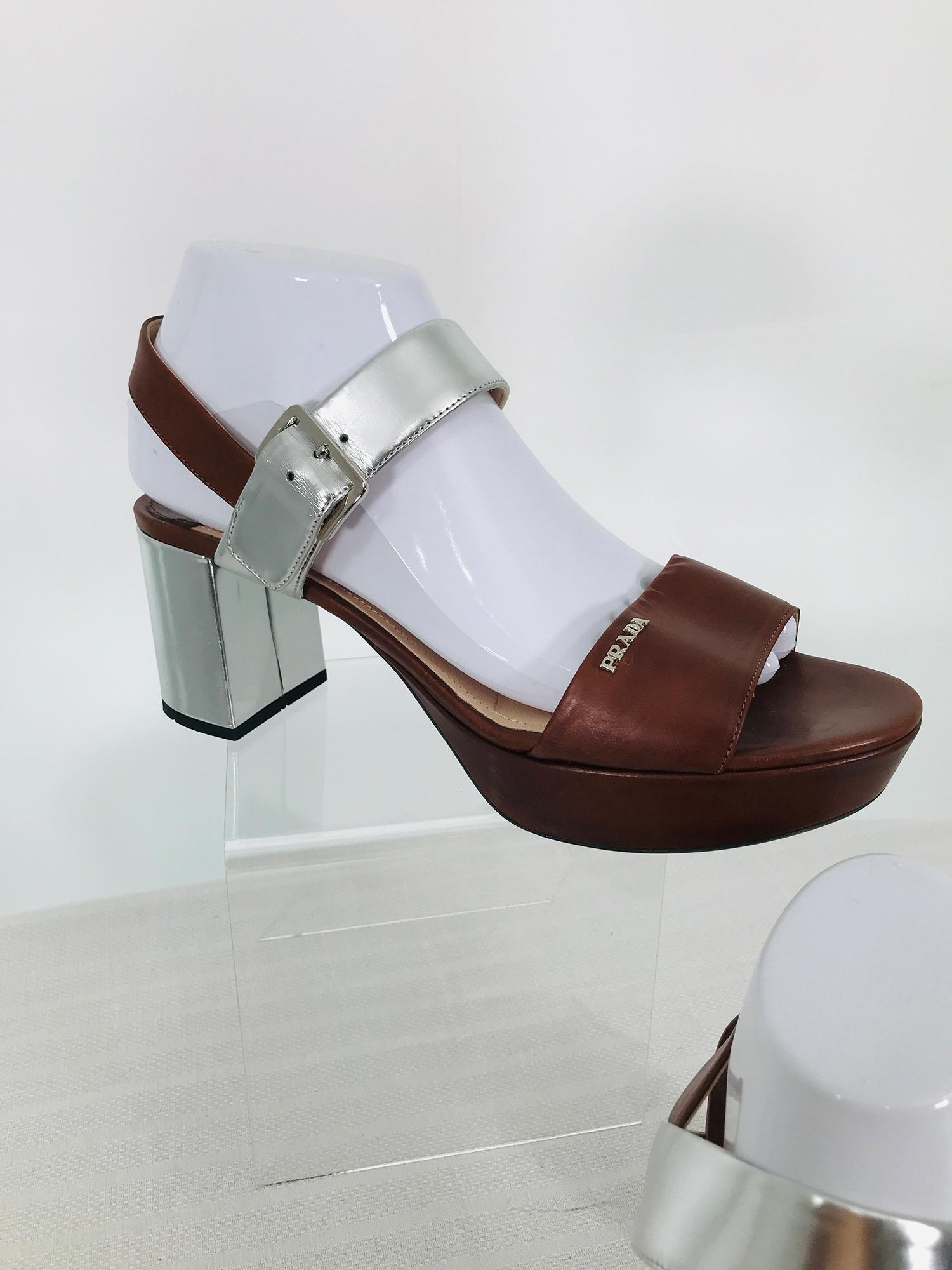 Prada ankle strap open toe platform sandals silver lamé heels & straps. Chocolate brown leather fronts the chunky heels and front ankle strap are silver lamé leather, silver metal buckles close at the ankle. There is a Prada silver metal signature