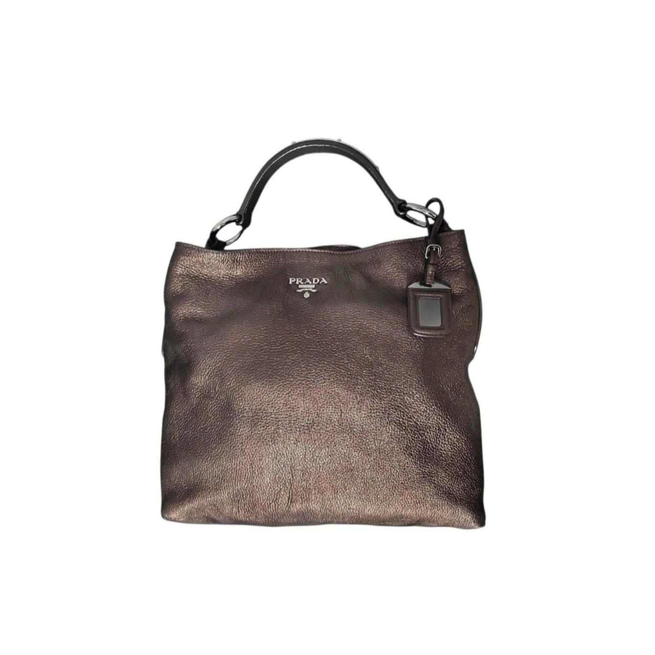 This Prada Vitello Daino Hobo in Antico Mordore is crafted of beautifully textured calfskin leather in metallic brown. This shoulder bag features a looping leather shoulder strap, polished silver hardware, and the classic polished silver metal