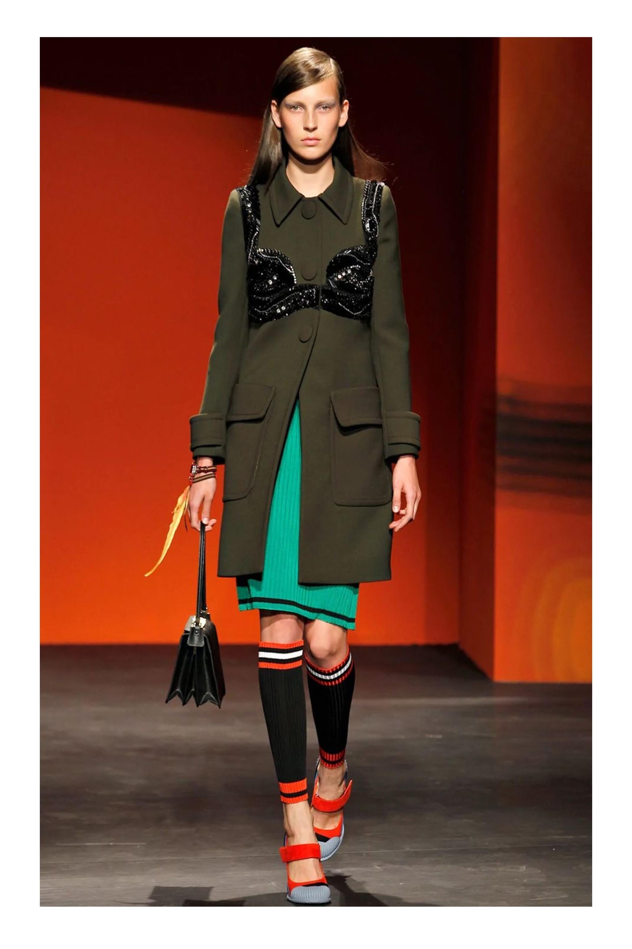 Resurrection Vintage se complace en ofrecer un abrigo de lana a medida verde militar de Prada con un intrincado detalle de abalorios negros de corpiño, botones de gran tamaño, grandes bolsillos con solapa, forro completo y largo hasta la