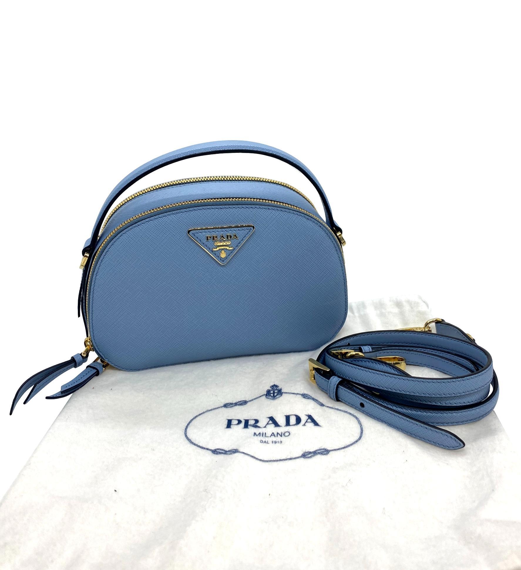 Prada Light Blue Saffiano Leather Odette Top Handle Cross-body Bag, 2020. Inspired by photographer's camera cases, the rounded shape of Prada's Odette bag is classic yet trendy for the new year. This bag was hand crafted in Italy from Prada's