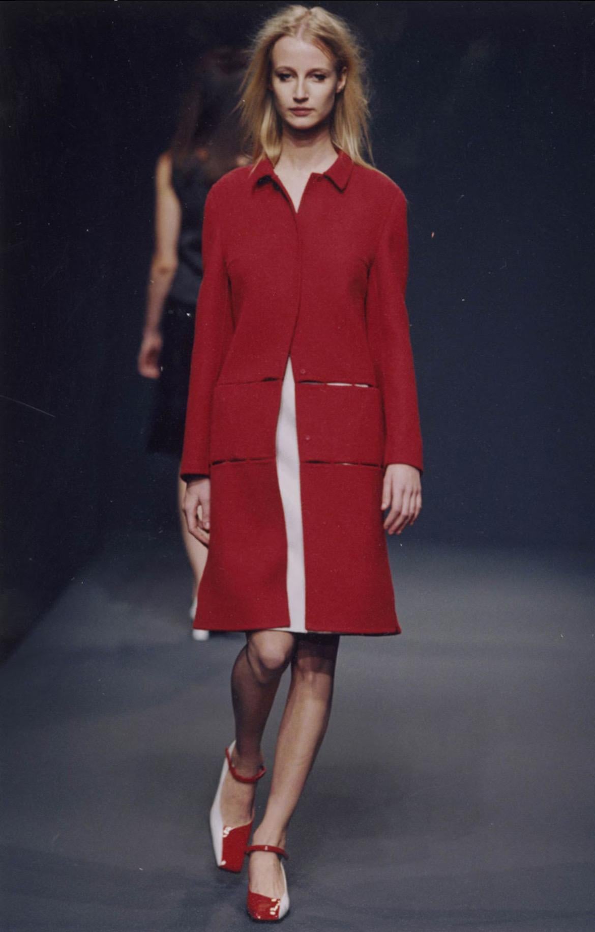 Prada Automne/Hiver 1998 manteau en laine rouge avec  panneaux cousus ouverts. Se ferme à l'aide de boutons-poussoirs.

Présenté sur le podium et dans la campagne.

Étiqueté taille 42.

Elle est en excellent état.