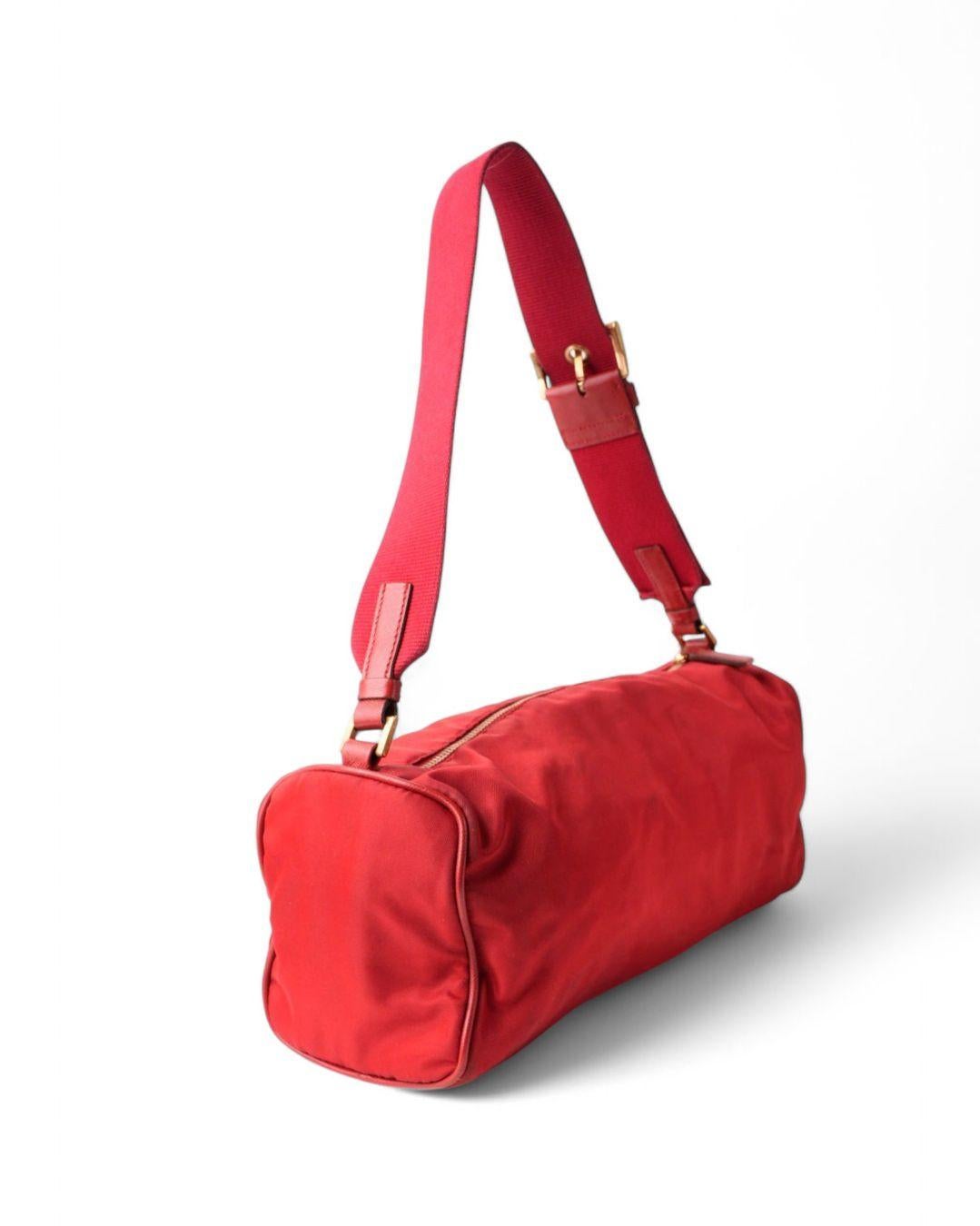 Borsa firmata Prada, modello Bassotto nella misura MM, realizzata in nylon rossa con rifiniture in tessuto e hardware neri. Dotata di una chiusura superiore a zip, internamente rivestita in tessuto nero logato con comoda tasca, la borsa è abbastanza