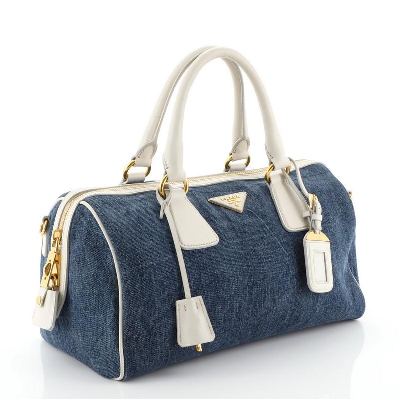 This Prada Bauletto Bag Denim with Saffiano Leather Medium, crafted from blue denim with saffiano leather, features dual rolled handles, Prada Milano logo, and gold-tone hardware. Its zip closure opens to a blue fabric interior with side slip