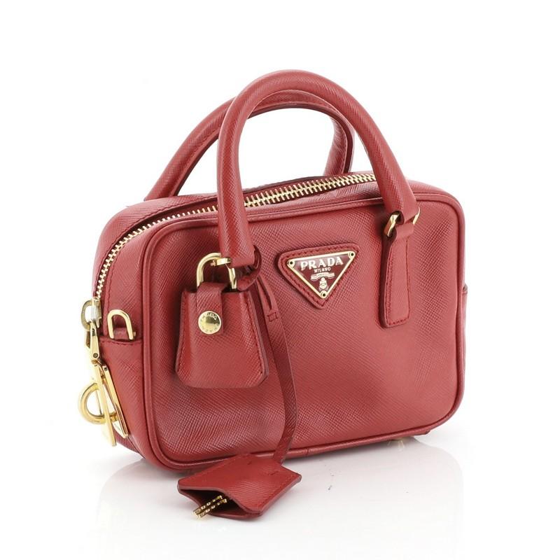 This Prada Bauletto Bag Saffiano Leather Mini, crafted from red saffiano leather, features dual-rolled tall handles, raised Prada Milano logo, and gold-tone hardware. Its top zip closure opens to a red fabric interior with side zip pocket.