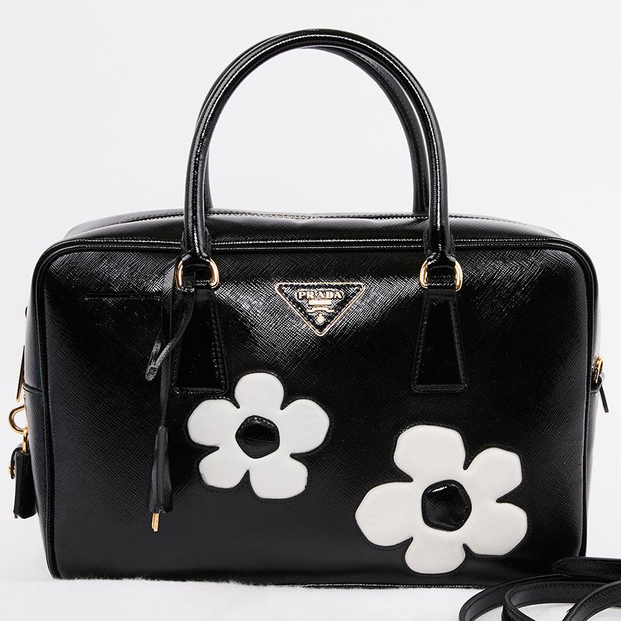 Magnificent second-hand PRADA bag in black patent Saffiano leather with two large inlaid white flowers on each side. It has a zipper. The lining is in 
