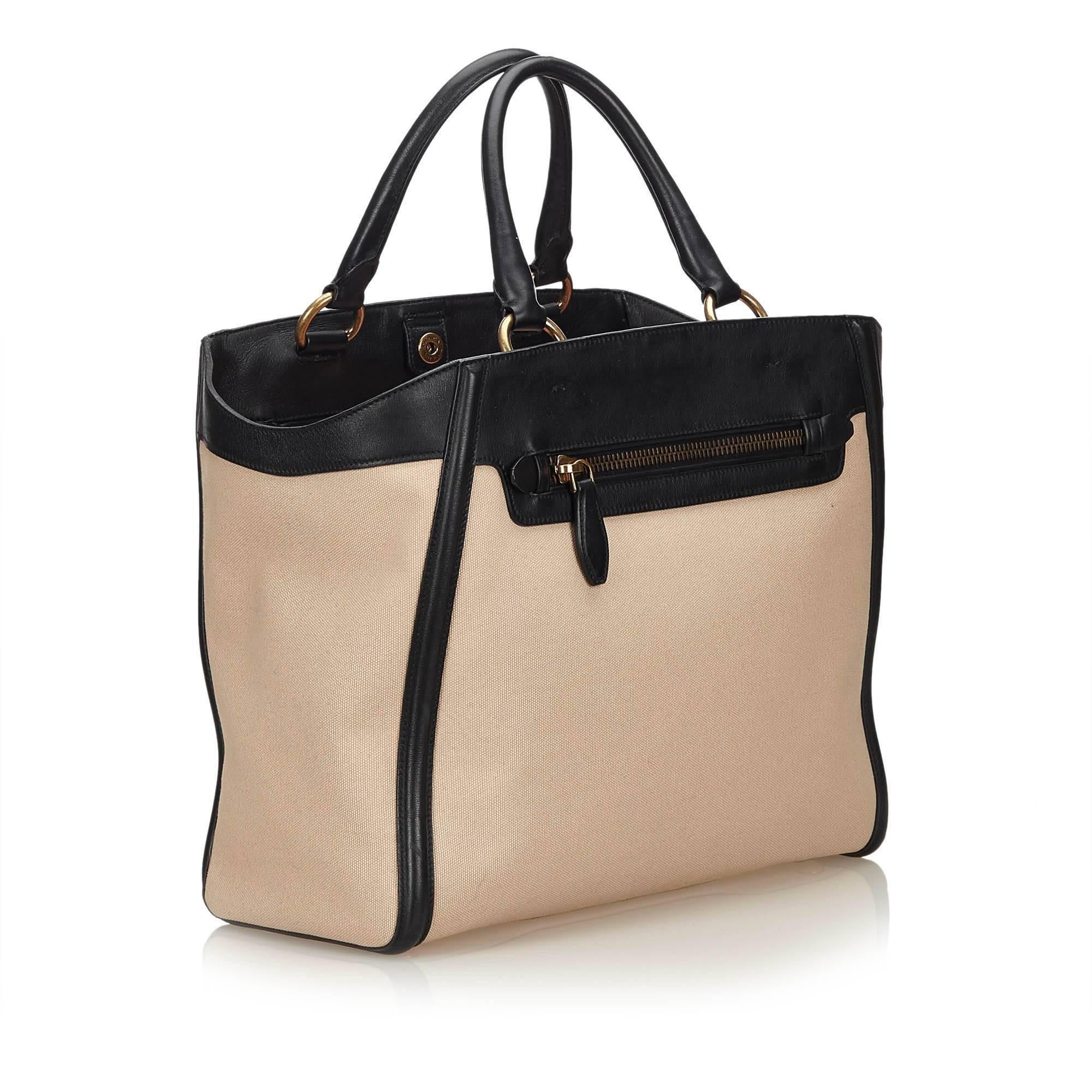 The tote bag features a canvas body with leather top panel and trim, rolled leather handles, open top with snap button closure, exterior zip pocket and interior zip, flap, and slip pockets. 

It carries an AB condition rating.

Dimensions: 
Length