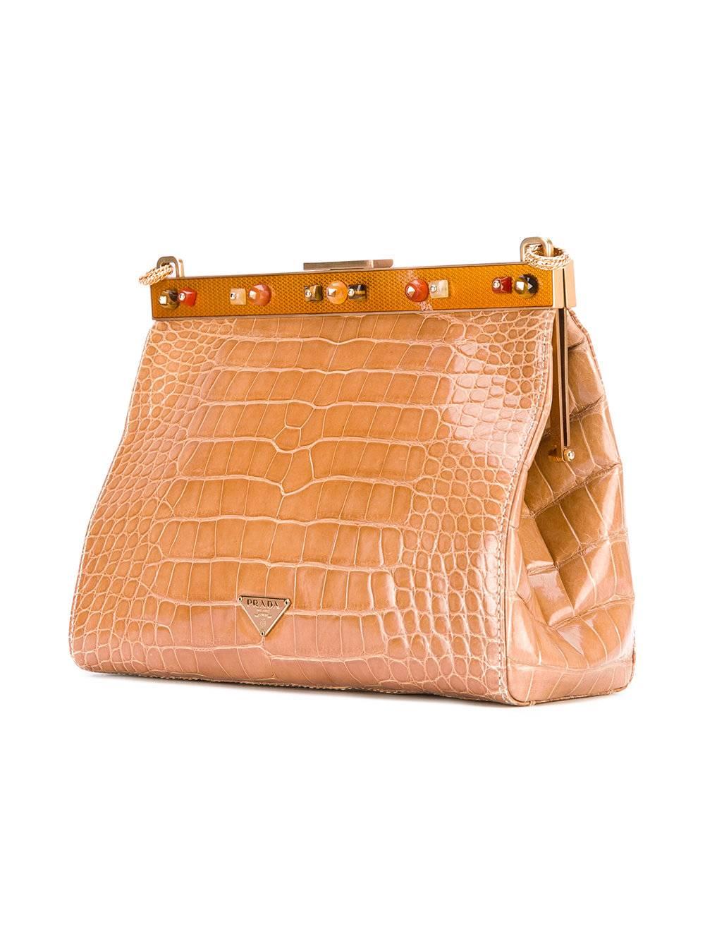 Marvelous dark beige crocodile leather chain clutch by Prada with orange glass and metal closure. It features a chain strap, a top magnetic closure, gemstone embellishments and an internal zipped pocket. The item is vintage, it was produced in the