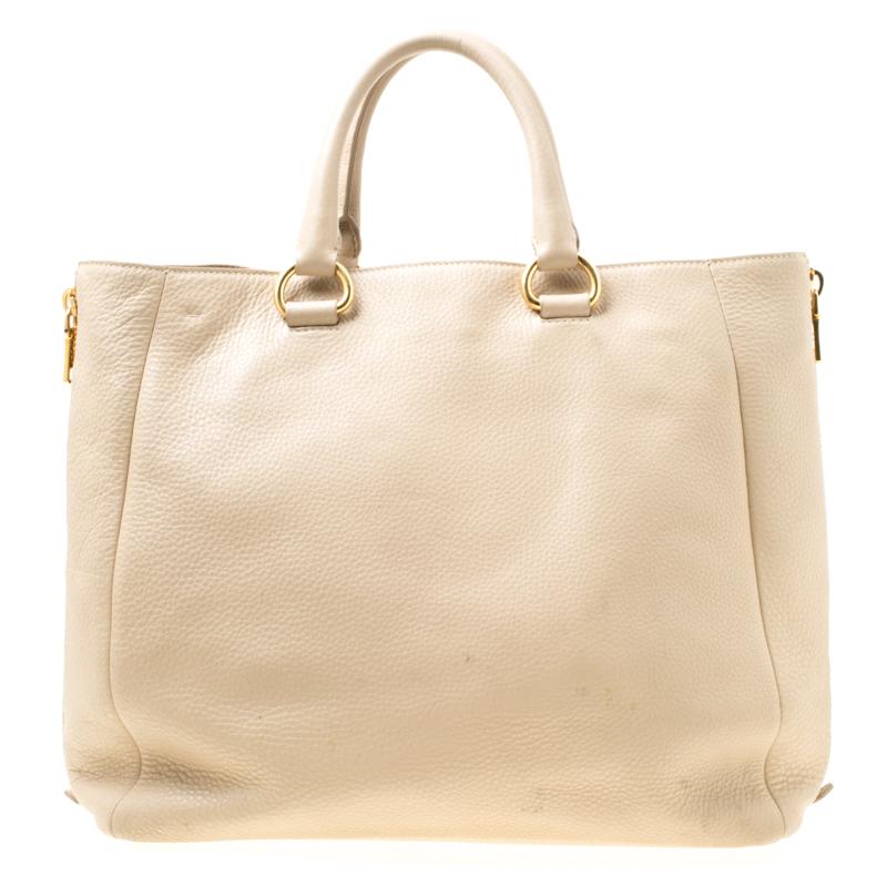 Prada brings you this tote that is overflowing with style. Covered in beige, the bag brings a spacious nylon interior to dutifully hold all your necessities and side zippers which can be unzipped to accommodate more things. Leather made, the bag is