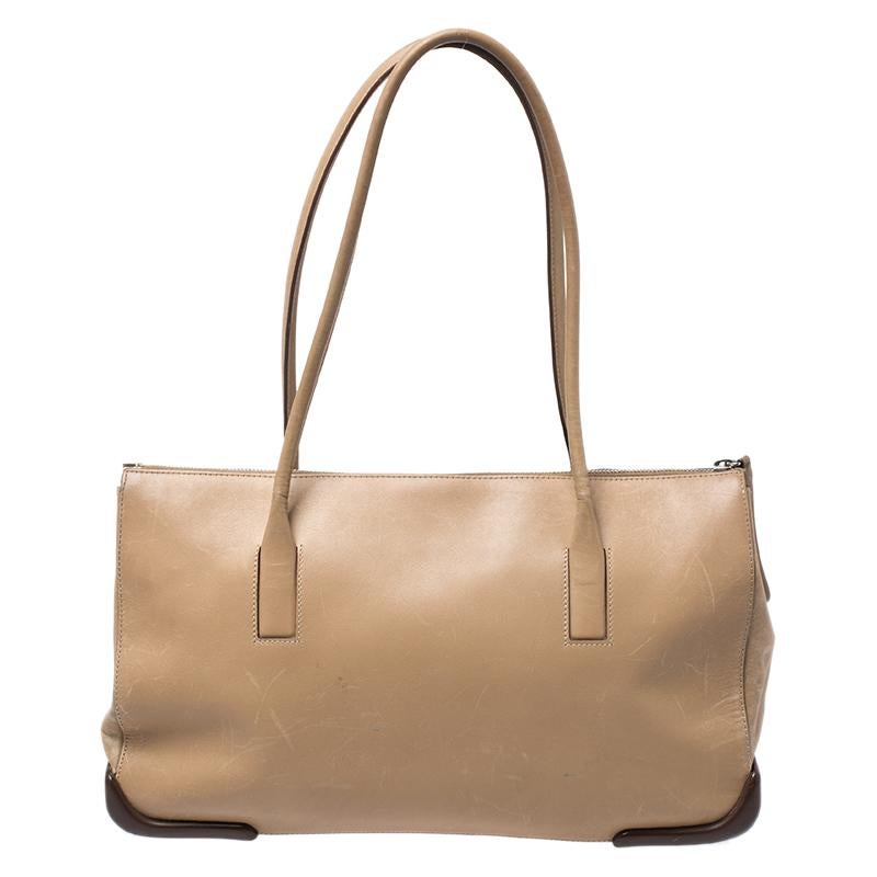 Elegant and classy, style your outfit with this beige tote from Prada. Crafted from leather, the tote comes with dual handles and a nylon interior secured by a zip closure. The tote is sure to hold your essentials and more.

