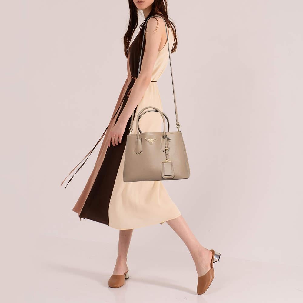 This designer tote from the House of Prada is super classy and functional perfect for everyday use. It is made from beige Saffiano Cuir leather with a logo accent adorning the front. It has two top handles.
