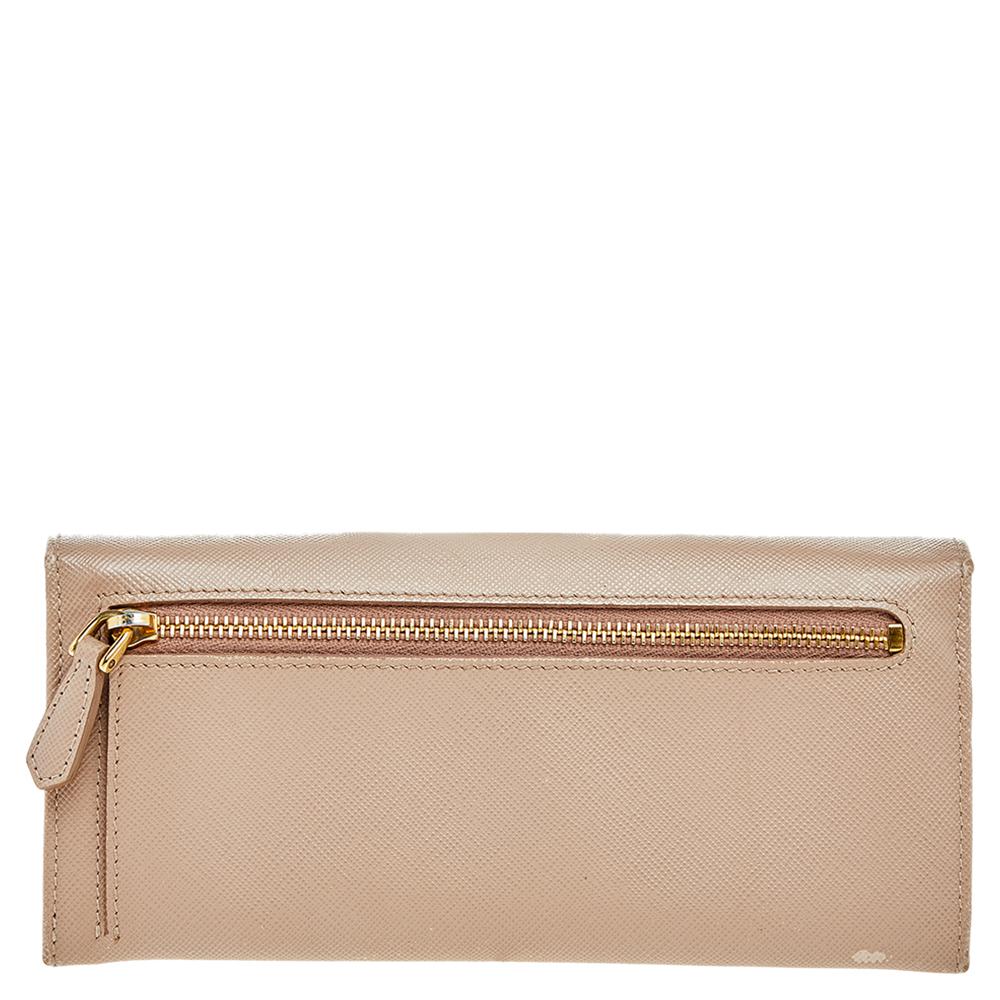 Funcionales y elegantes, las colecciones de Prada capturan la delicadeza desenfadada y sin esfuerzo de la mujer moderna. Confeccionada en piel saffiano de color beige, esta elegante cartera presenta un interior compartimentado con solapa decorada