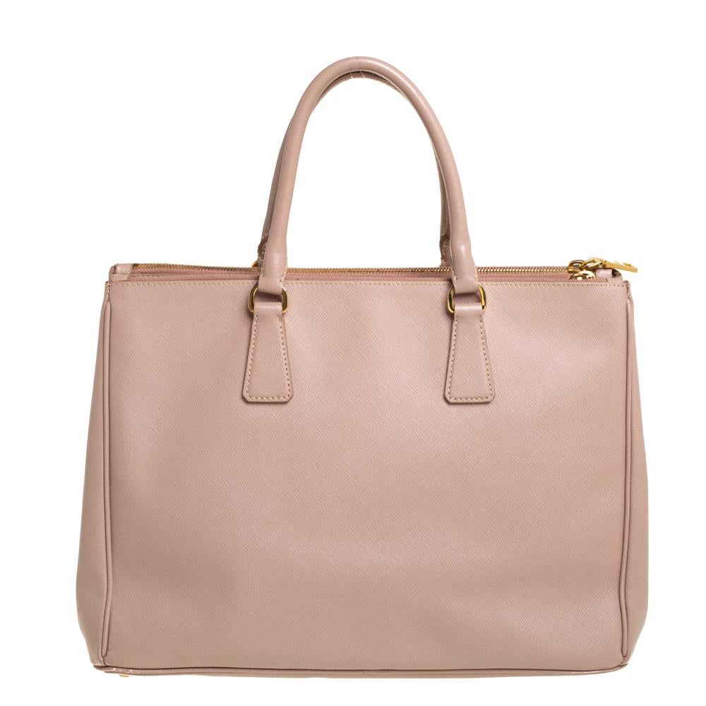 Femenino en forma y diseño, este bolso tote Galleria Double Zip de Prada será un complemento muy querido en tu armario. Se ha confeccionado en piel saffiano y se ha decorado mínimamente con herrajes dorados. Tiene dos asas superiores, compartimentos