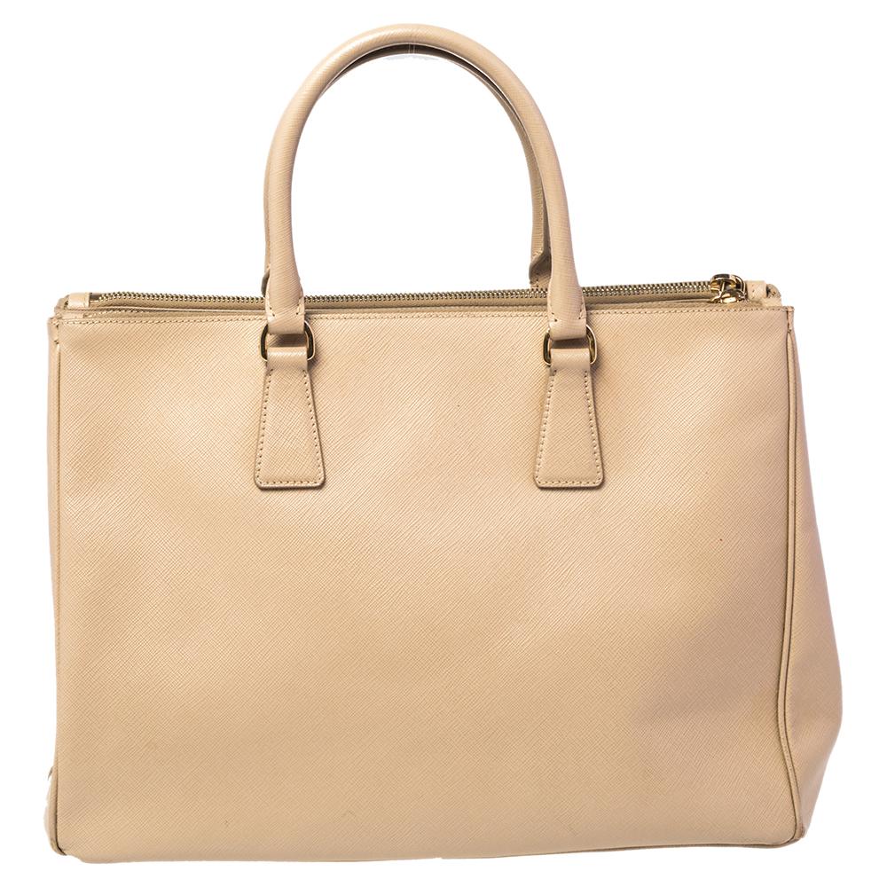 Loved for its classic appeal and functional design, the Galleria is one of the most popular bags from the house of Prada. This beauty in beige is crafted from Saffiano Lux leather and is equipped with two top handles, the brand logo at the front,