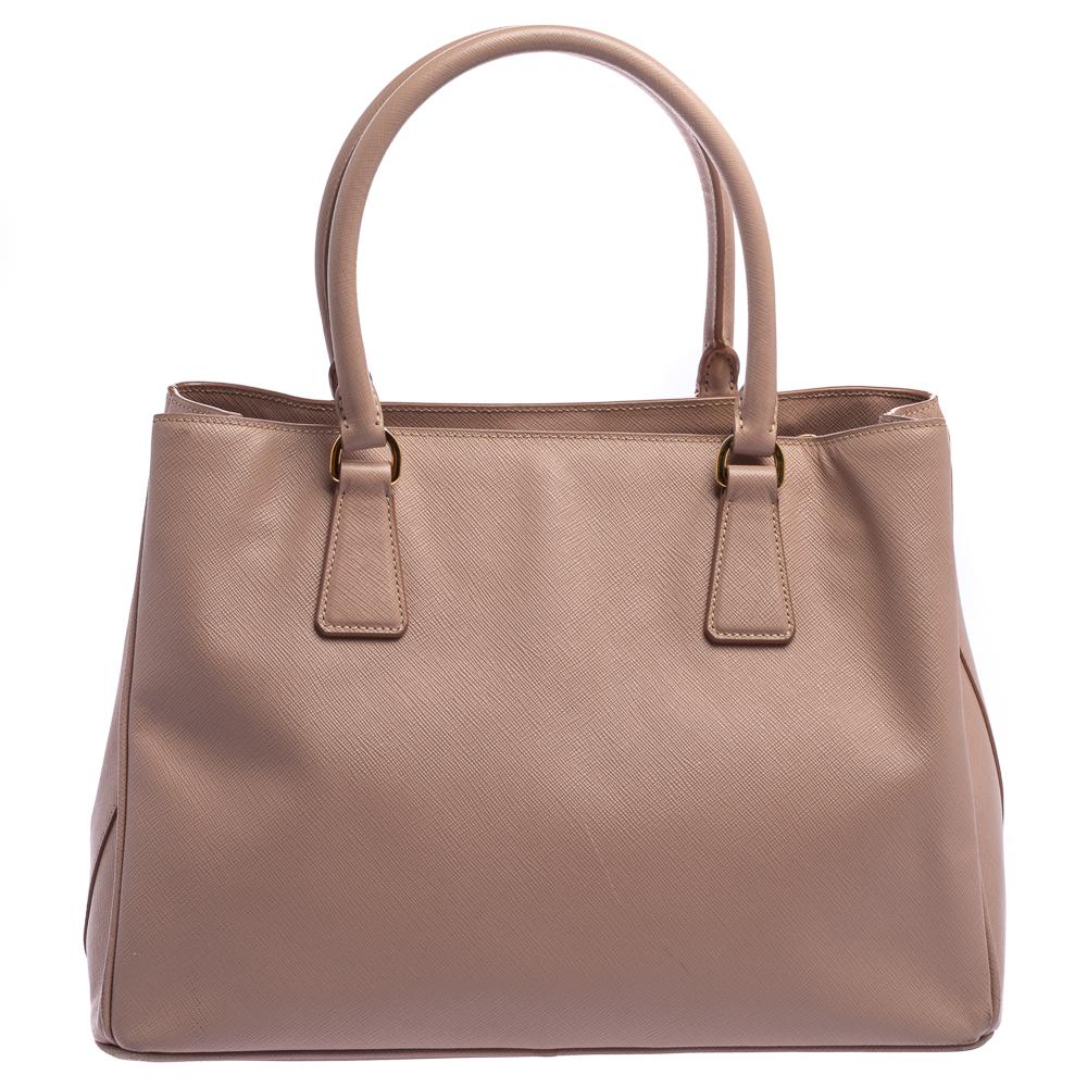Masterfully crafted using beige Saffiano Lux leather, this bag will make a loved addition. The Prada bag is held by two handles, equipped with metal feet and a nylon interior, and finished with the logo on the front. This is a one-stop fashion