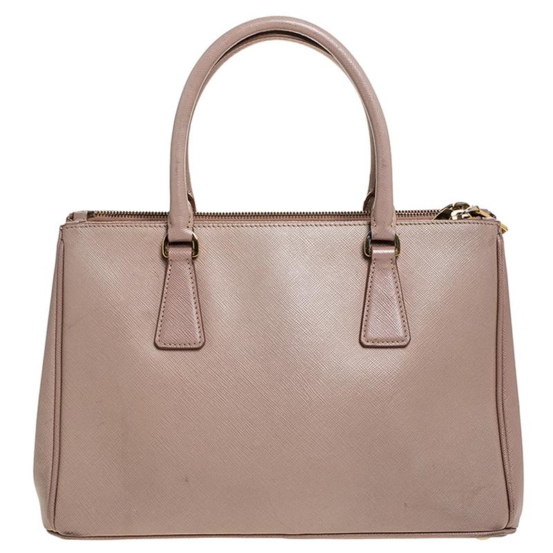 Be the talk of the town and let the others follow your style while you carry this adorable Prada Double zip tote. Made in Italy from beige Saffiano lux leather, this small-sized beauty comes equipped with double zipper pockets, dual-rolled short