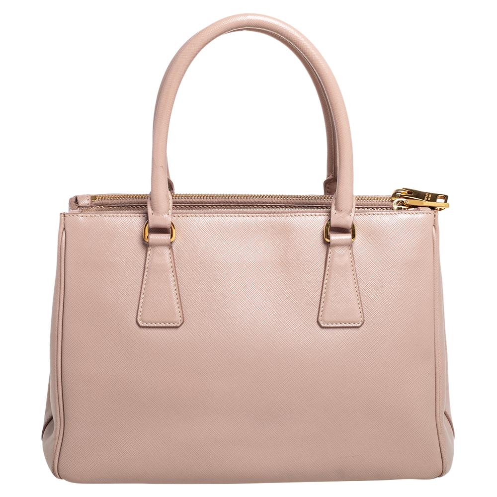 Die Galleria ist eine der kultigsten und beliebtesten Taschen aus dem Hause Prada und wird für ihre klassische Ausstrahlung und ihr funktionales Design geliebt. Diese beigefarbene Schönheit ist aus Saffiano-Leder gefertigt und mit zwei Henkeln an