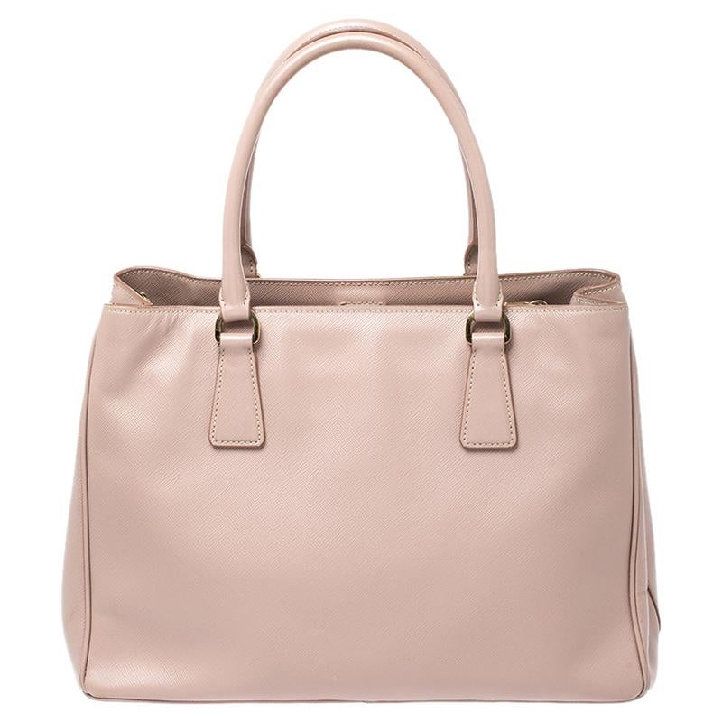 Sophisticated and timeless, this practical Saffiano Lux tote by Prada was made for daily use. Crafted from Saffiano leather in a beautiful shade of beige, the exterior features a Prada logo emblem at the front, rolled double top handles, a gold-tone