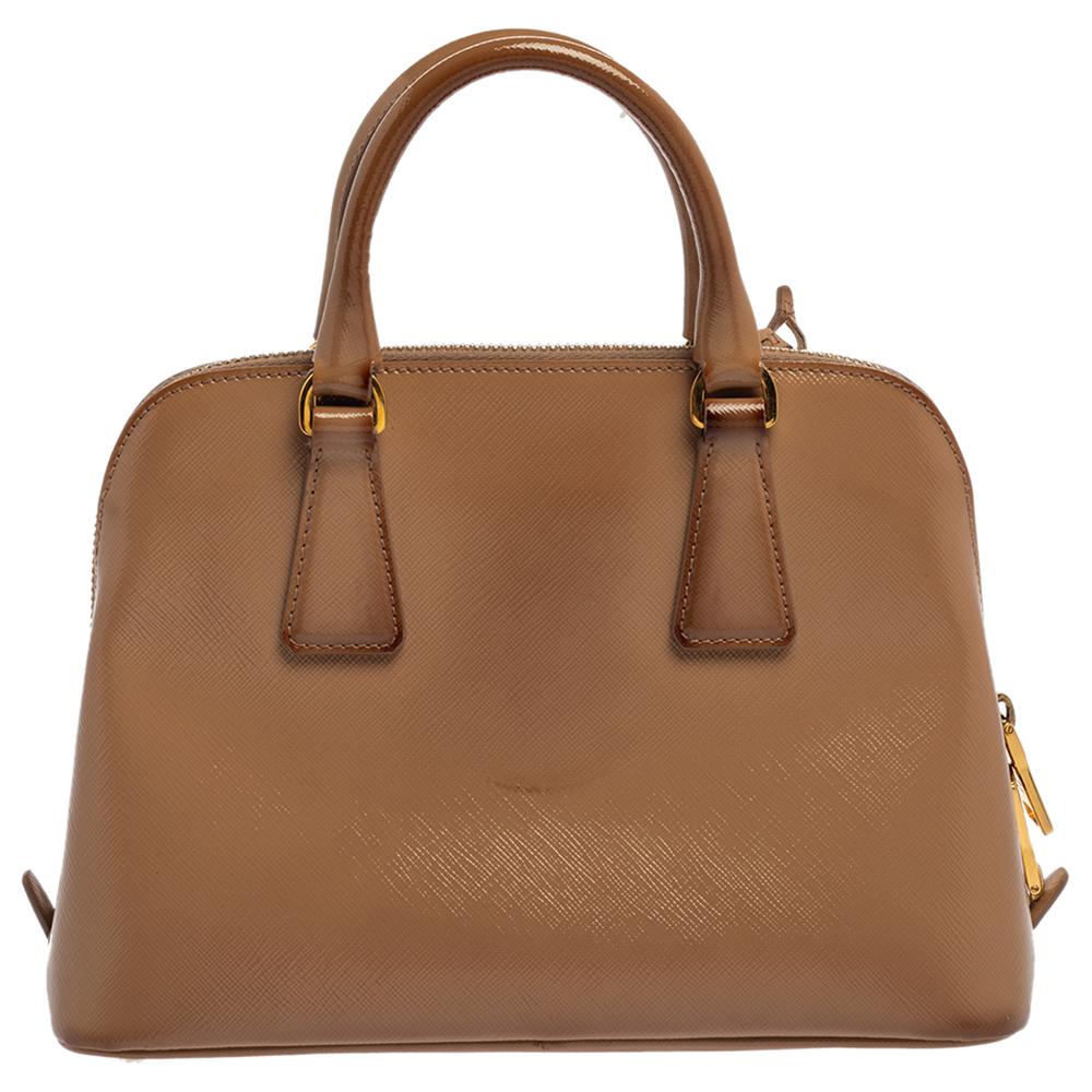 The Promenade is one of Prada's most loved styles when it comes to handbags. Grand in beige, the bag is crafted from Saffiano Lux patent leather and features two handles. The zip closure leads way to a nylon interior with enough space for your