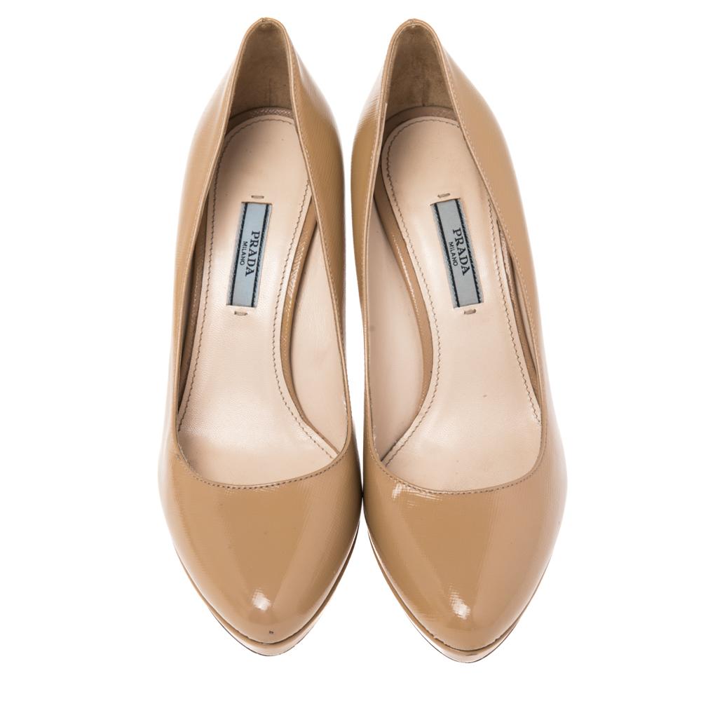 You can never go wrong with these classic pumps from the house of Prada. Crafted from Saffiano patent leather, they come in a neutral shade of beige. They are styled with round toes, platforms, 10 cm heels and gold-tone hardware. They are finished