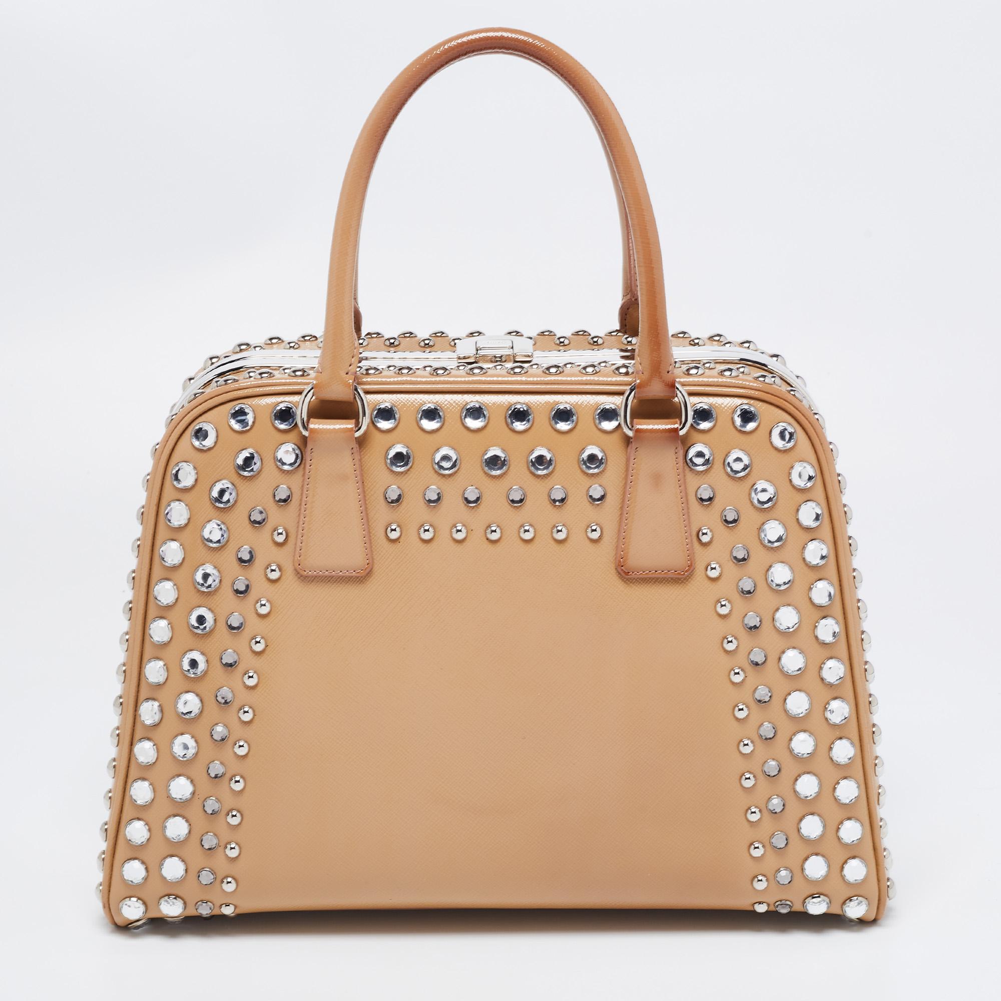 Giving handle bags an elegant update, this Pyramid Frame satchel by Prada aims to be a valuable addition to your closet. It is crafted from Saffiano patent leather and styled with studded embellishments. It comes with dual top handles, protective