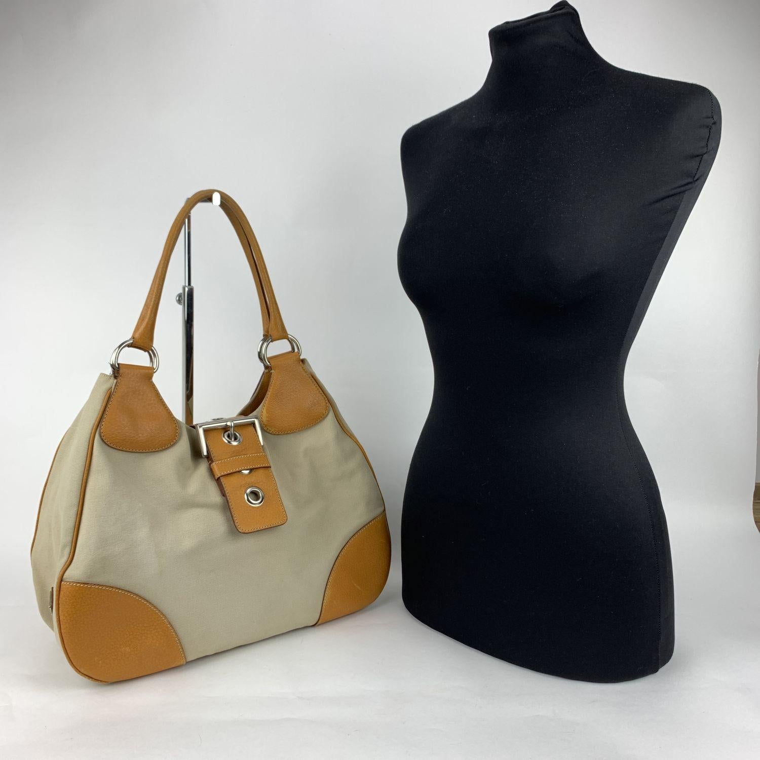 PRADA Tessuto Buckle Hobo . Contemporary design and an edgy bold look. Beige 'Tessuto' canvas and tan leather trim . Fold over strap belt with buckle detail . Silver metal hardware. PRADA signature lining . 1 side zip pocket inside.PRADA triangle