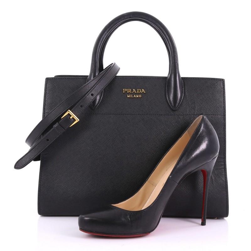 This Prada Bibliotheque Handbag Saffiano Leather with City Calfskin Medium, crafted from black saffiano leather, features dual rolled leather handles, expandable concertina sides, and gold-tone hardware. It opens to a black leather interior with