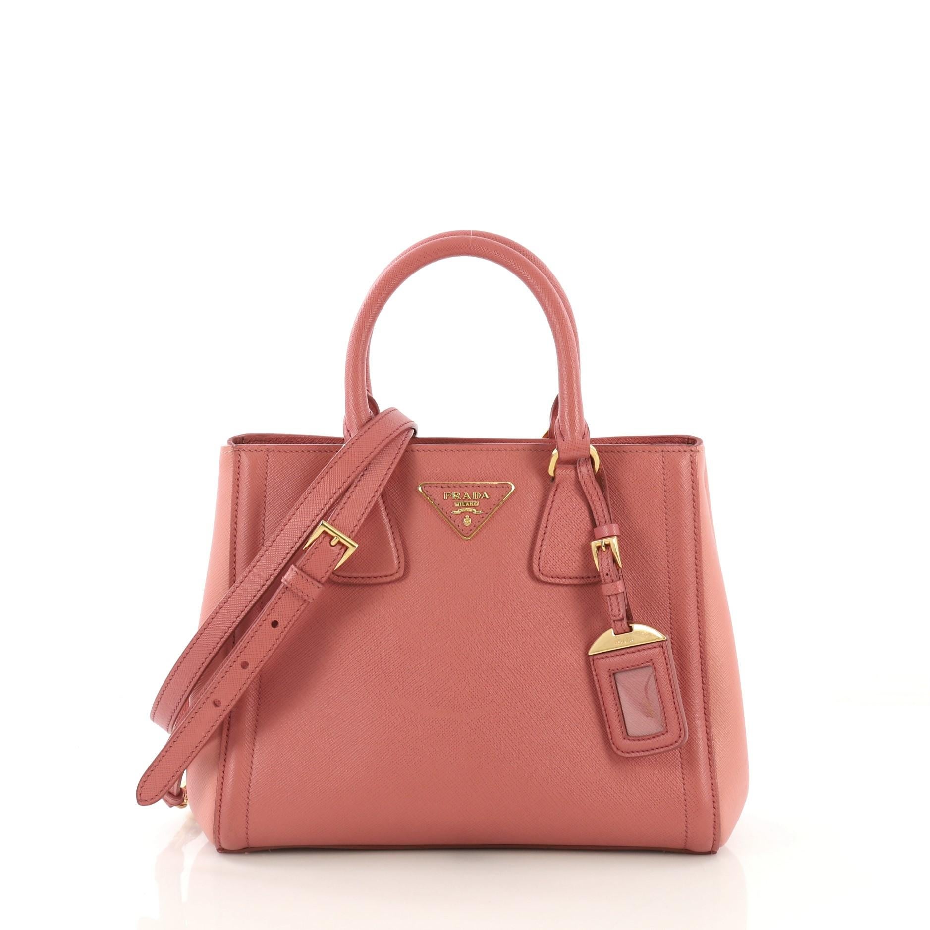 This Prada Bicolor Lux Convertible Open Tote Saffiano Leather Small, crafted in pink saffiano leather, features dual rolled leather handles, side snap buttons, protective base studs, and gold-tone hardware. Its snap button closure opens to a pink