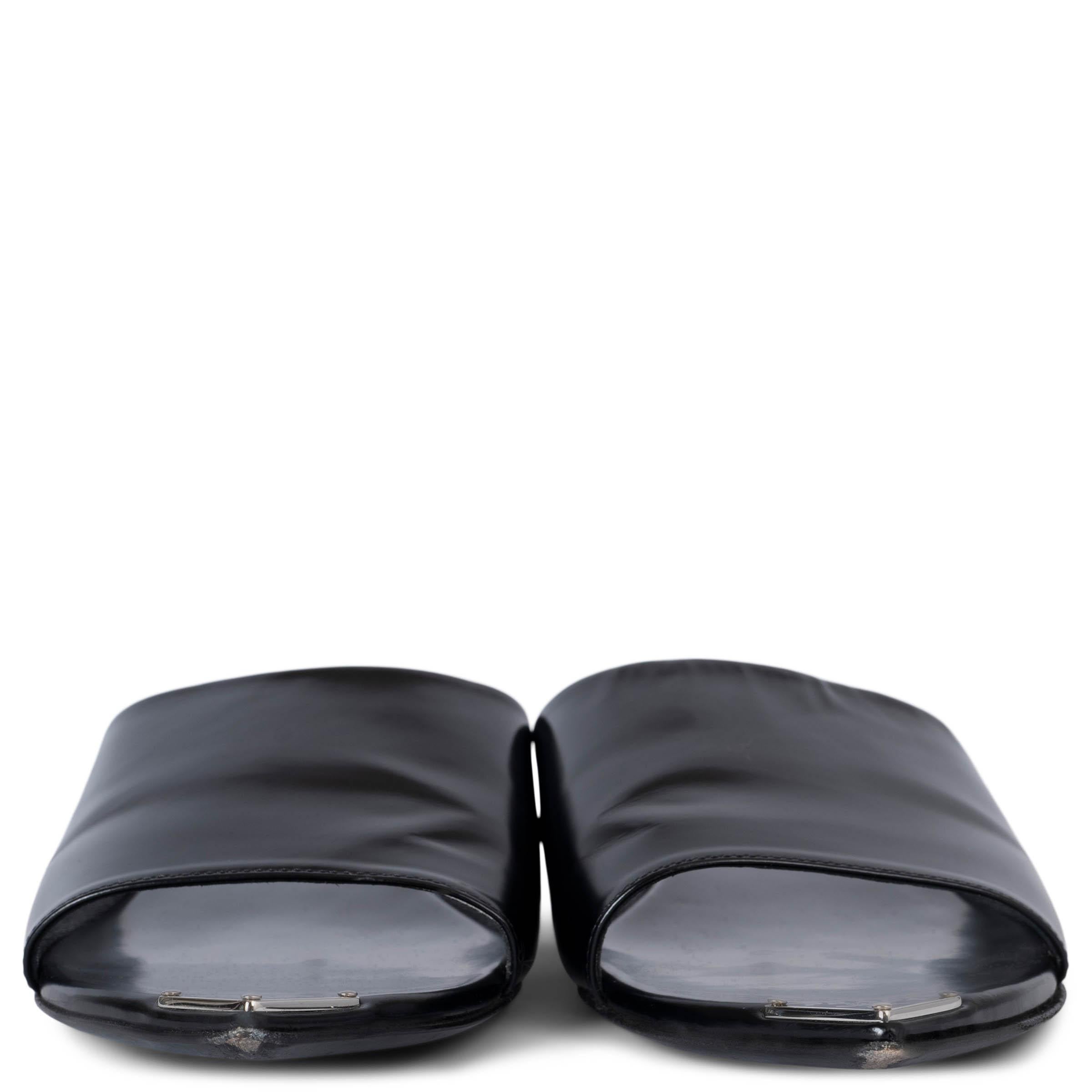 Estas sandalias 100% auténticas de Prada están confeccionadas en piel de becerro cepillada negra. Presentan una puntera puntiaguda con una placa triangular esmaltada con el logotipo y una correa ancha, combinando un diseño depurado con una elegancia