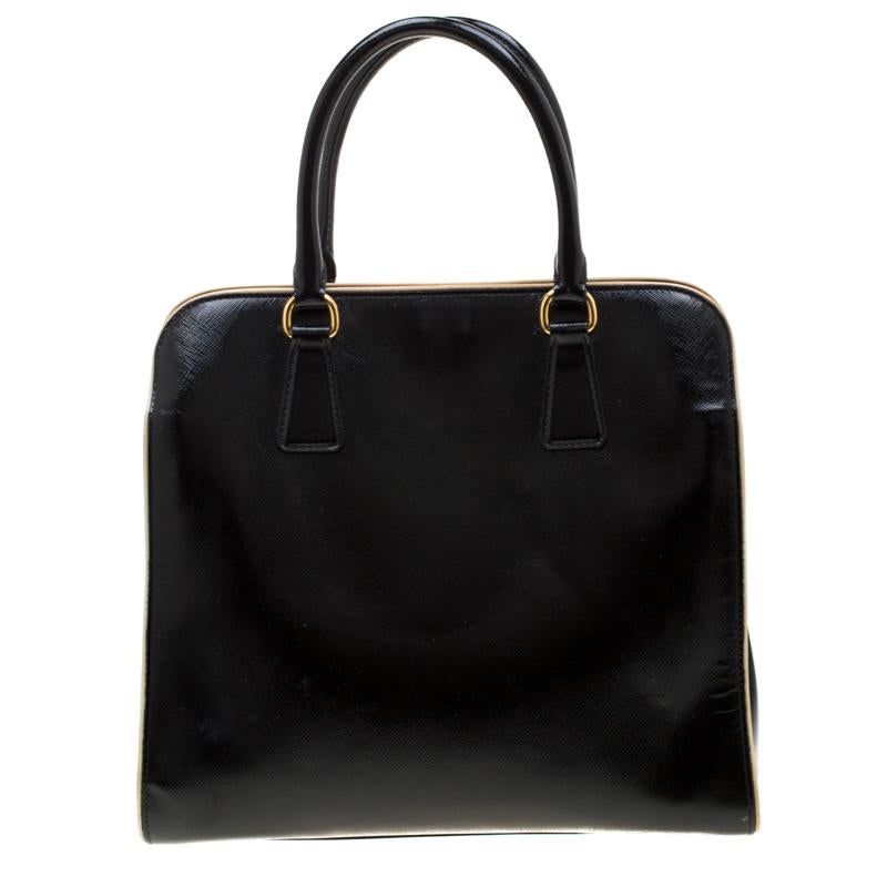 Giving handle bags an elegant update, this Pyramid bag by Prada will be a valuable addition to your closet. It has been crafted from black patent leather into a structured silhouette with contrasting cream-colored outlines. It comes with dual top