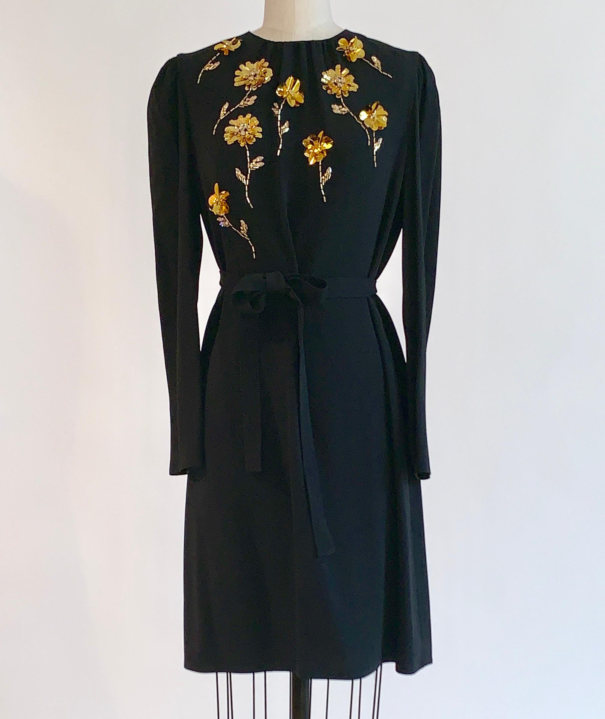 2016 Prada black long sleeve dress with gold beaded flower pattern and tie belt. Slightly puffed sleeve at shoulder. Back zip and hook and eye.

72% acetate, 28% viscose.
Fully lined  (except for sleeves) in 60% cupro, 40% silk.
Made in Italy.

Size